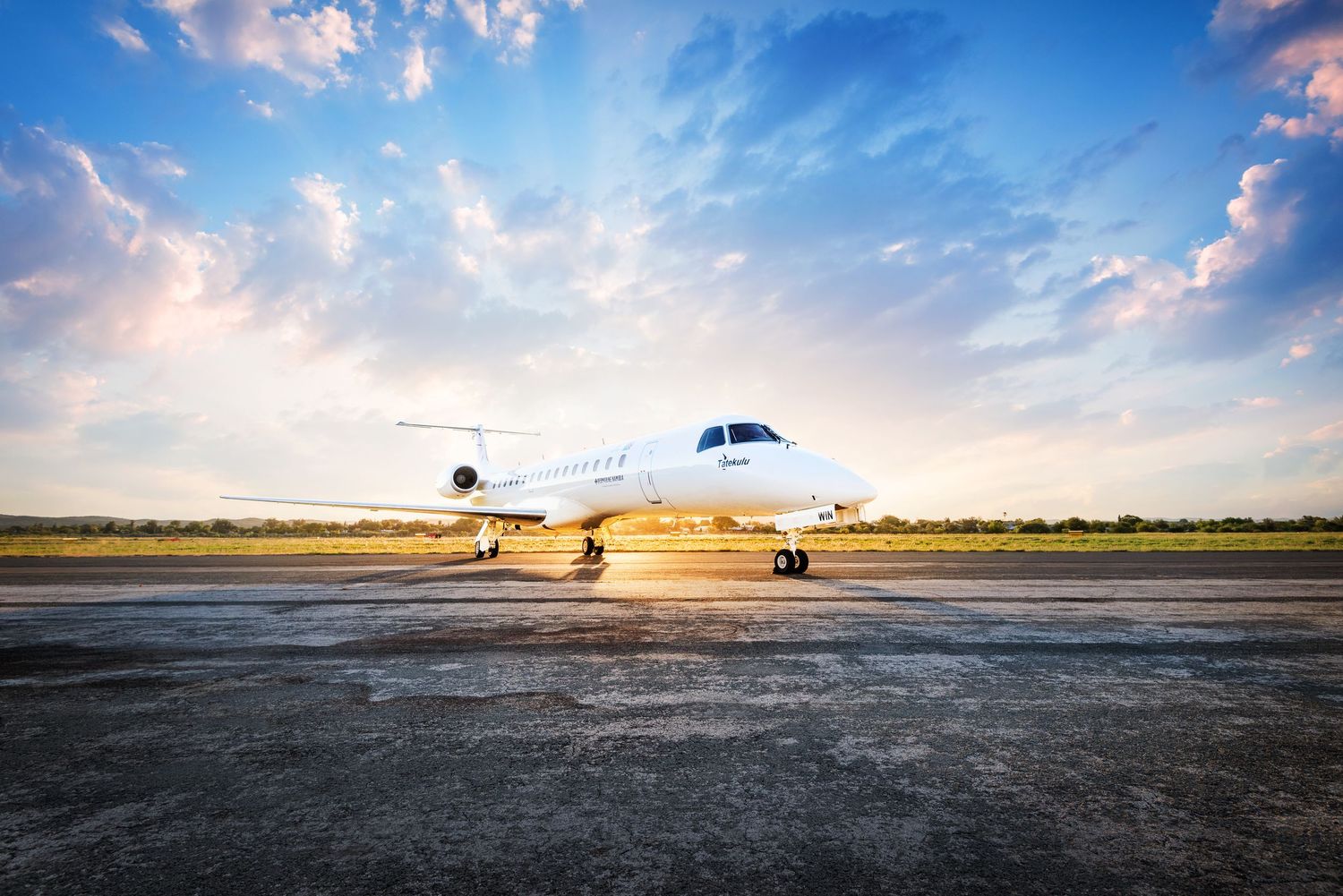 White private jet parked on tarmac at sunset with dramatic blue sky and clouds in the background.