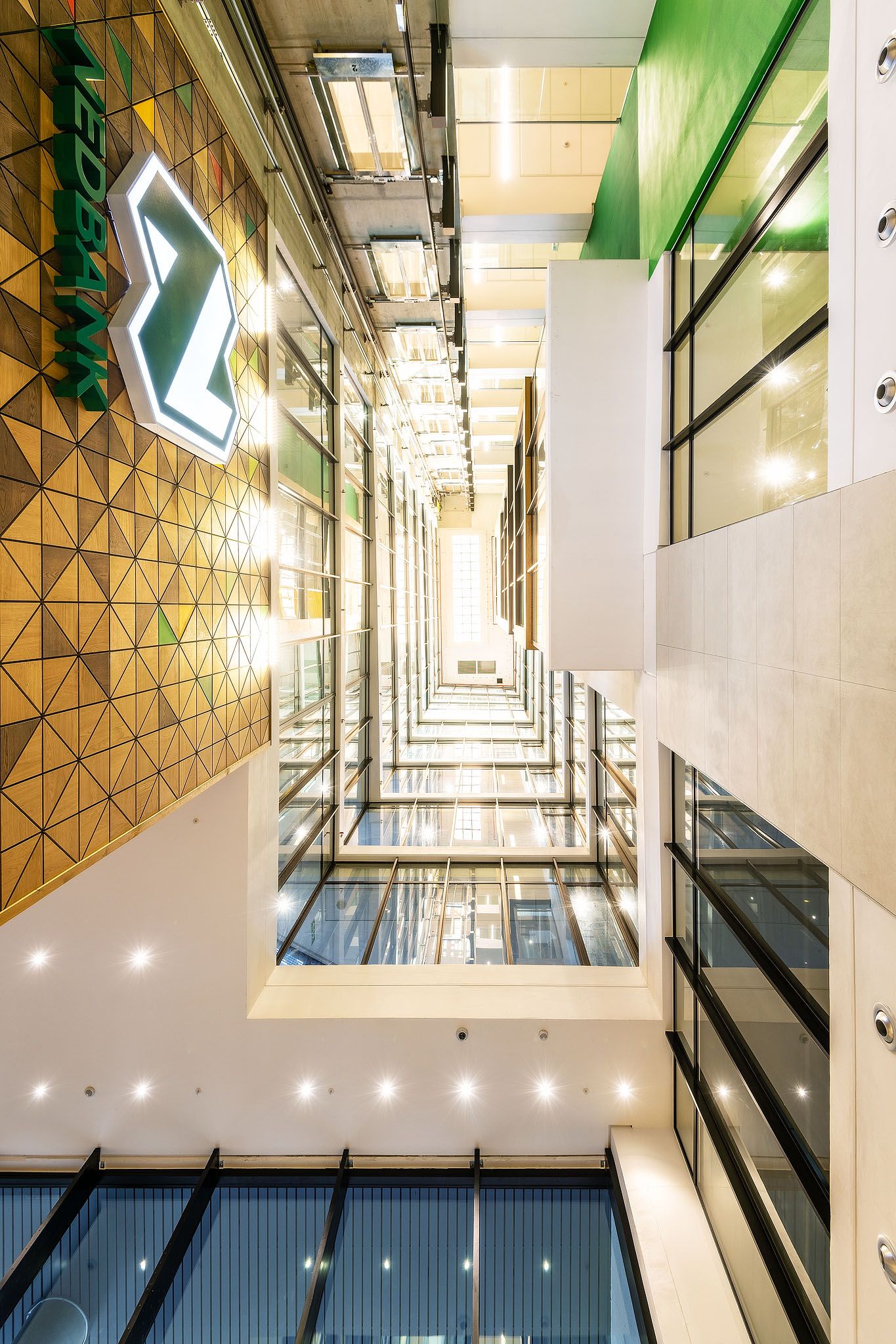 Looking up through a dramatic multi-story glass atrium with gold geometric wall panels in modern office.