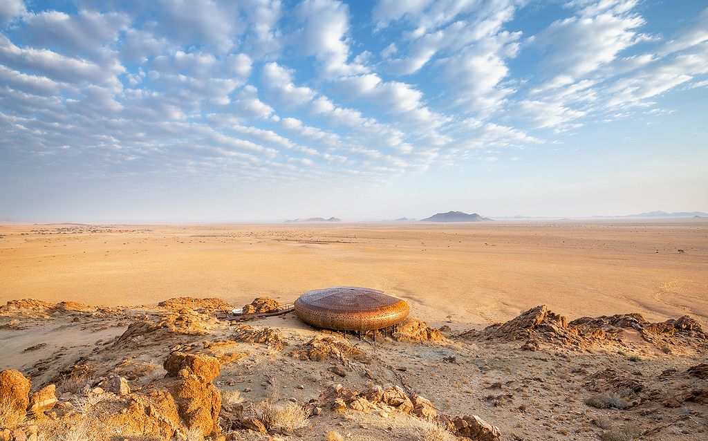 Solitary futuristic dome structure sitting atop a rocky desert plateau under dramatic cloudy skies in Namibia.