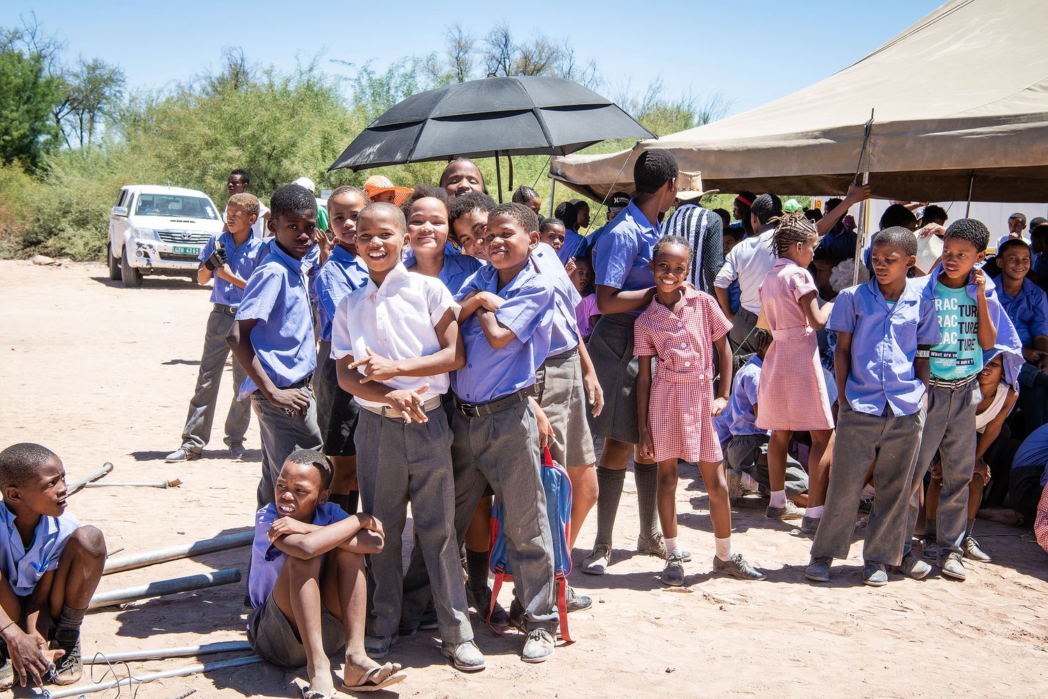 Group of African schoolchildren in blue uniforms gathered outdoors at a school event on a sunny day.
