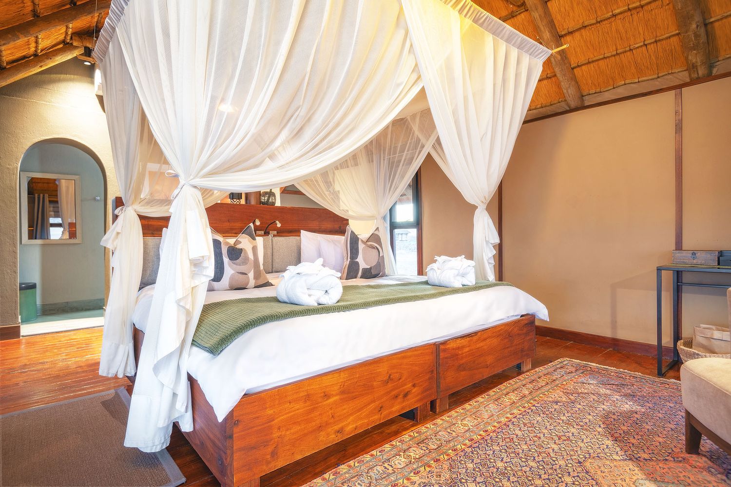Romantic safari suite with canopy four-poster bed, thatched ceiling, and warm wooden furnishings.
