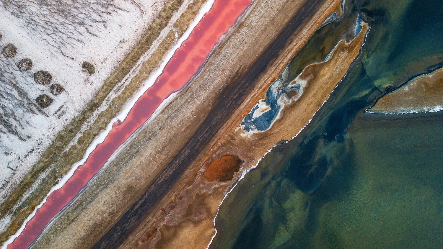 Aerial view of colorful shoreline with pink, teal, and brown hues along a coastal road in winter.