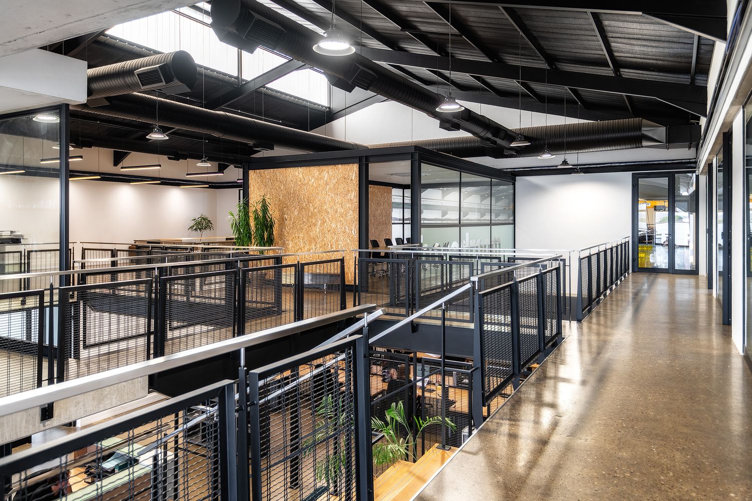Modern industrial office mezzanine with black steel railings, polished concrete floors, and open workspace below flooded with natural light.
