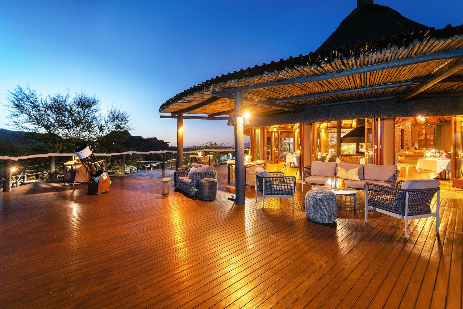 Elegant safari lodge deck with plush seating and panoramic views at twilight in the African wilderness.