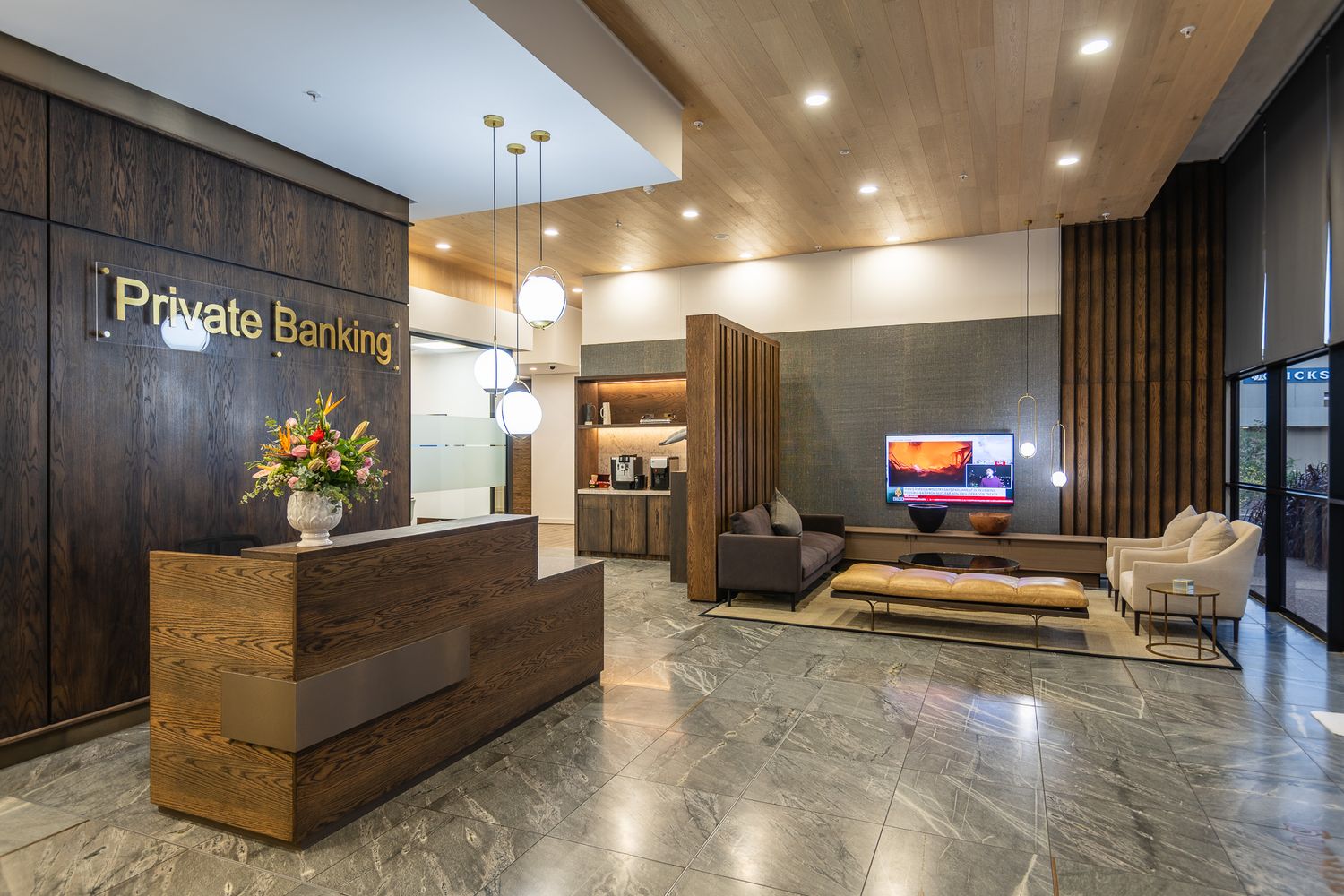 Elegant private banking lobby with wooden reception desk, marble floors, pendant lights, and modern lounge seating area.