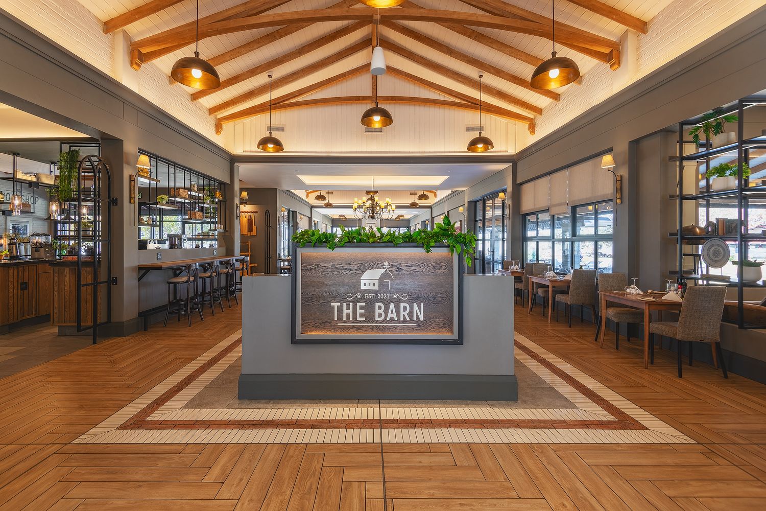 Elegant entrance to The Barn restaurant featuring warm wood floors, vaulted ceiling with pendant lights, and modern farmhouse decor.