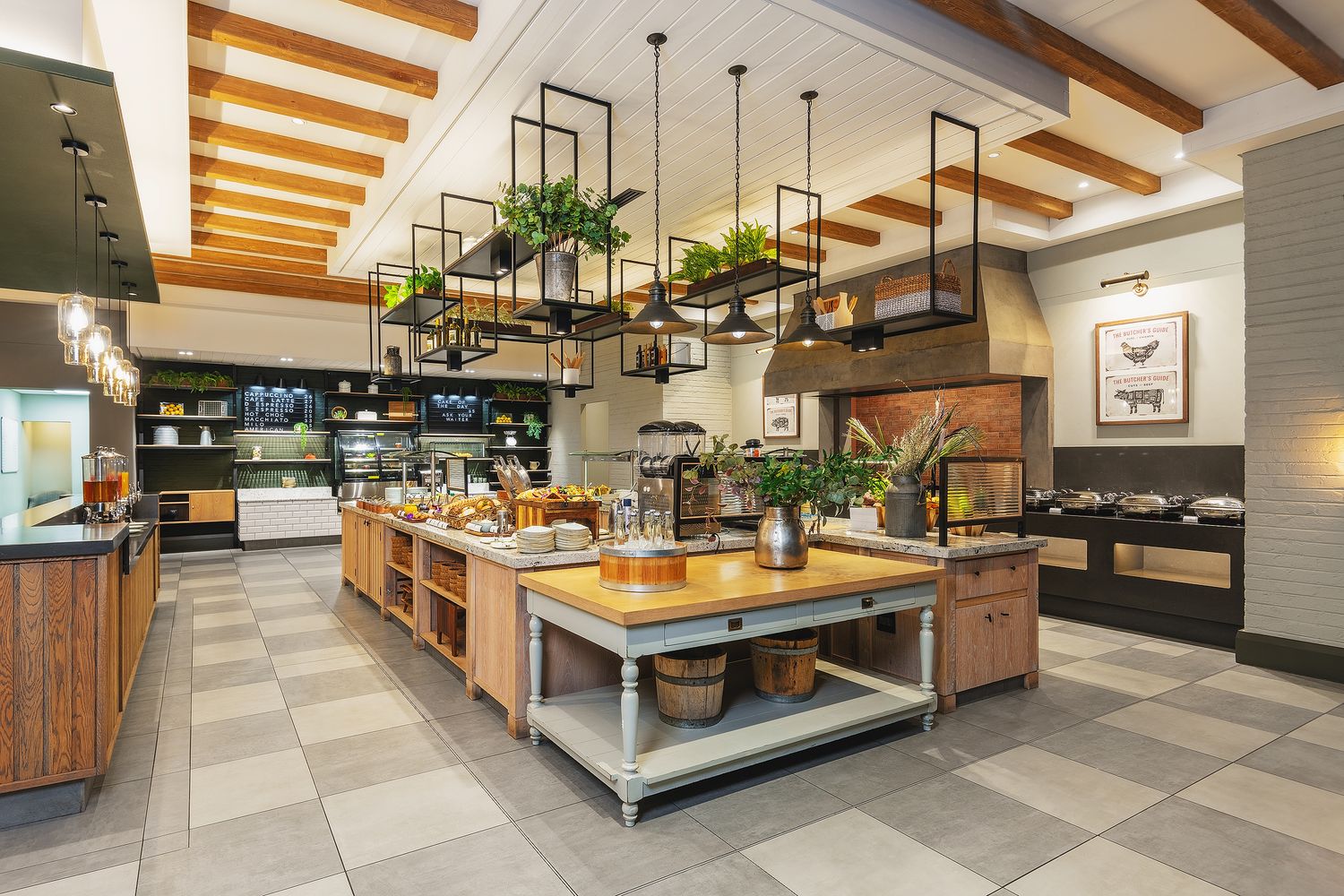Modern restaurant kitchen with wooden island, hanging plants, pendant lights, and open shelving in a bright, airy space.