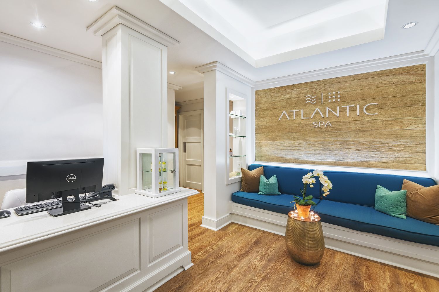 Elegant Atlantic Spa reception area featuring a blue velvet bench, white desk, gold accents, and warm wood flooring.