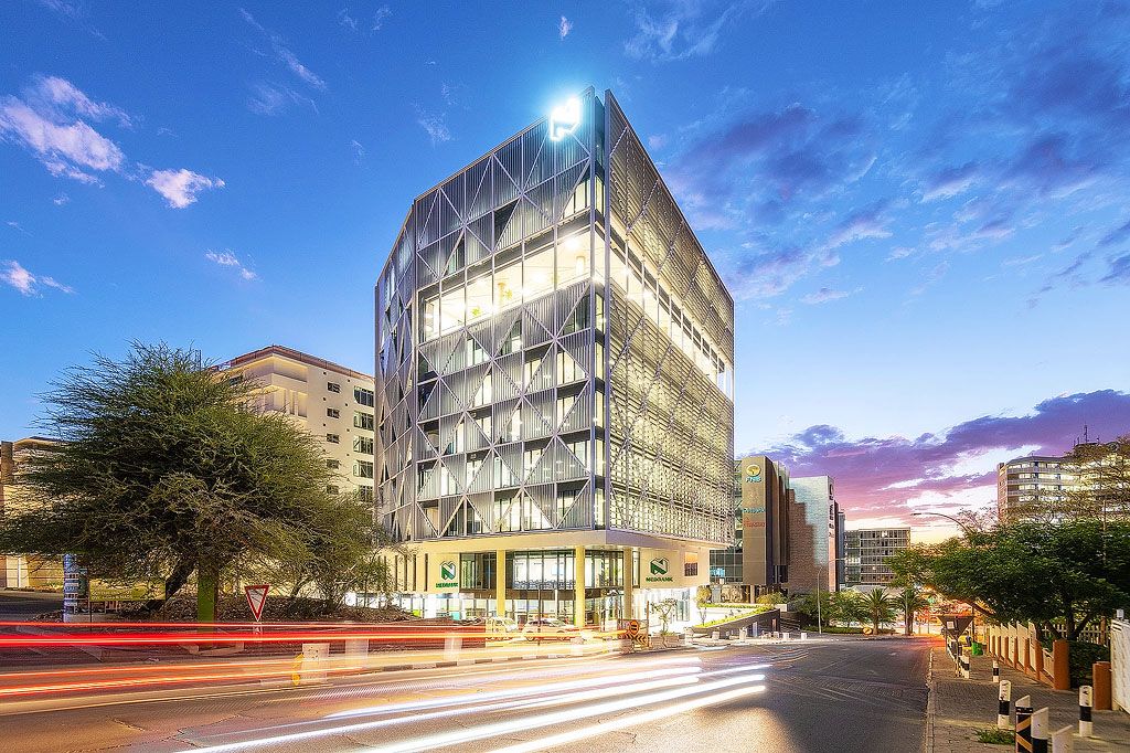 Modern glass office building illuminated at dusk with light trails from passing traffic in urban Johannesburg.