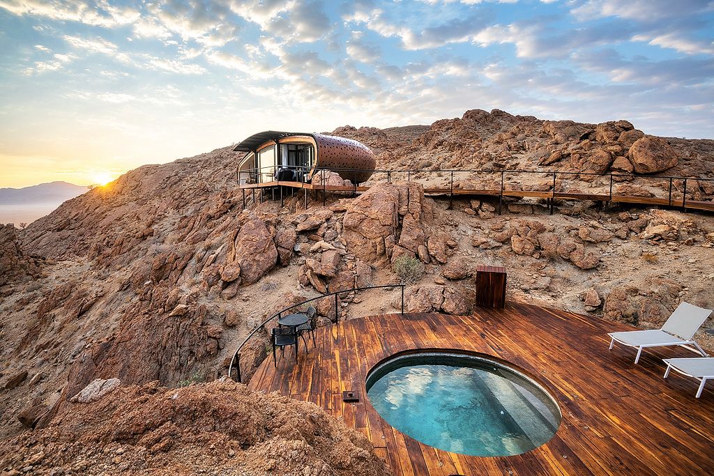 Unique pod-shaped luxury suite on rocky desert hillside with private wooden deck and plunge pool at sunset.