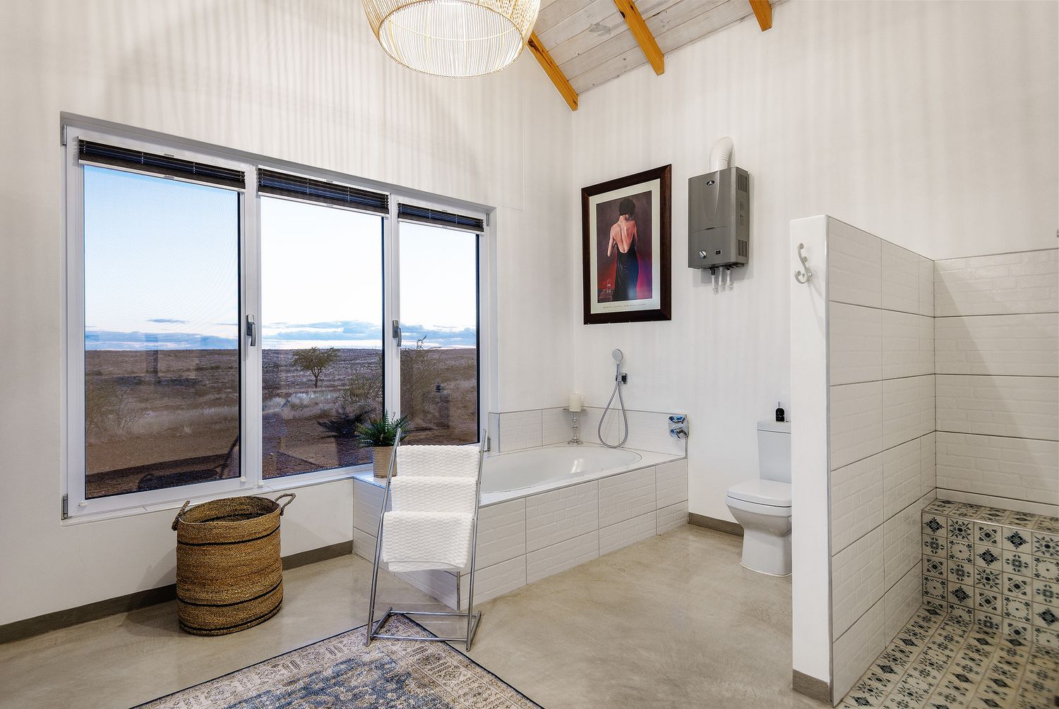 Bright white bathroom with soaking tub, large window with scenic views, walk-in shower, and decorative rug on concrete floors.