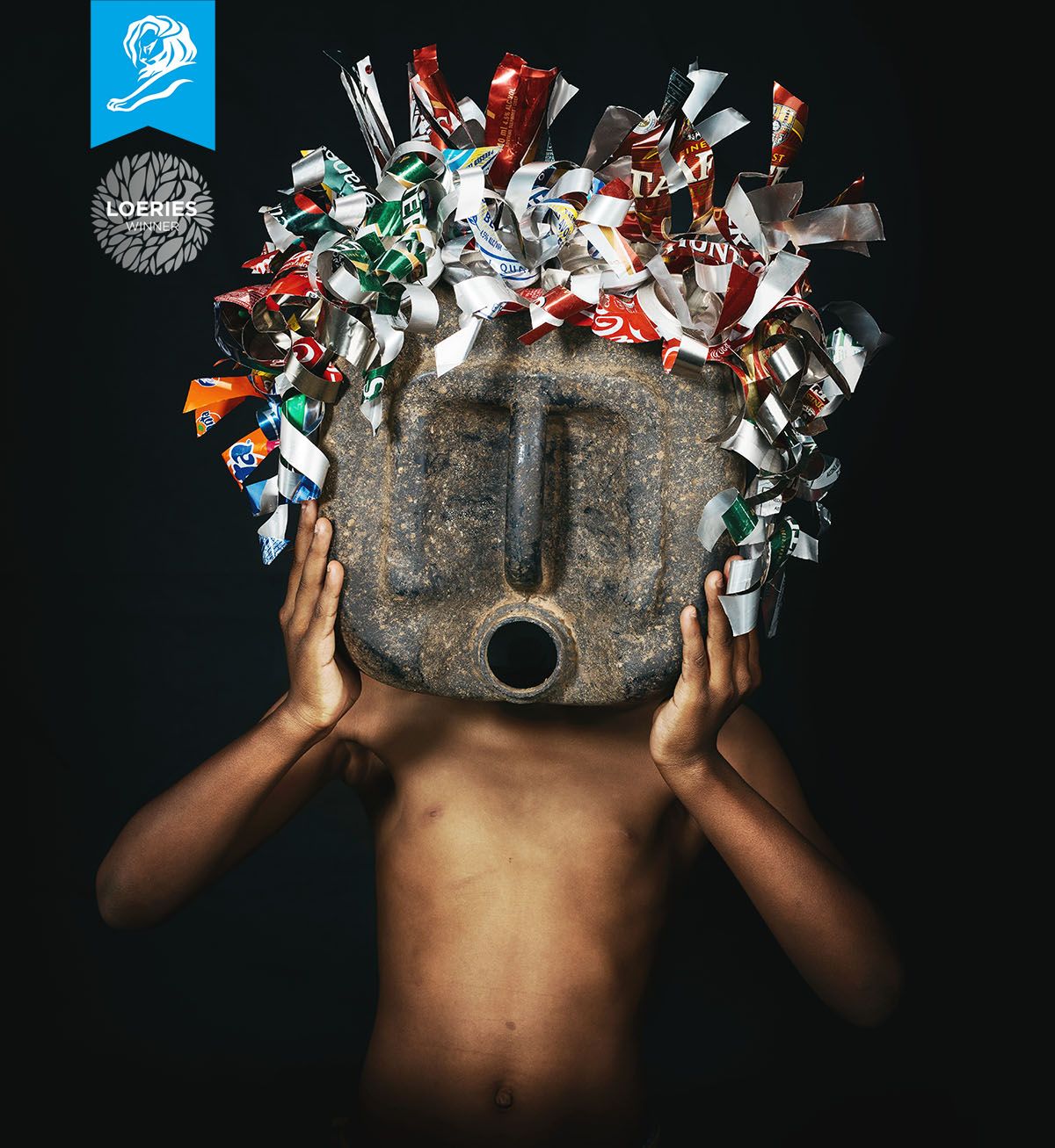 Child holding stone mask decorated with colorful plastic waste, symbolizing environmental pollution impact.
