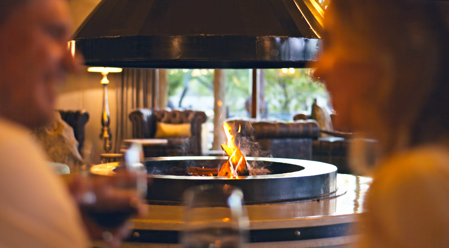 Couple dining near a circular open fireplace in an elegant restaurant with warm ambient lighting.