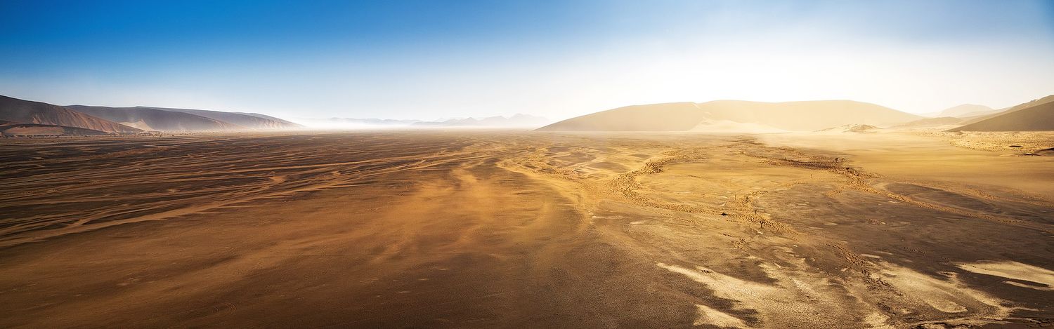 Aerial panoramic view of a vast arid desert landscape with golden sand dunes under a clear blue sky.