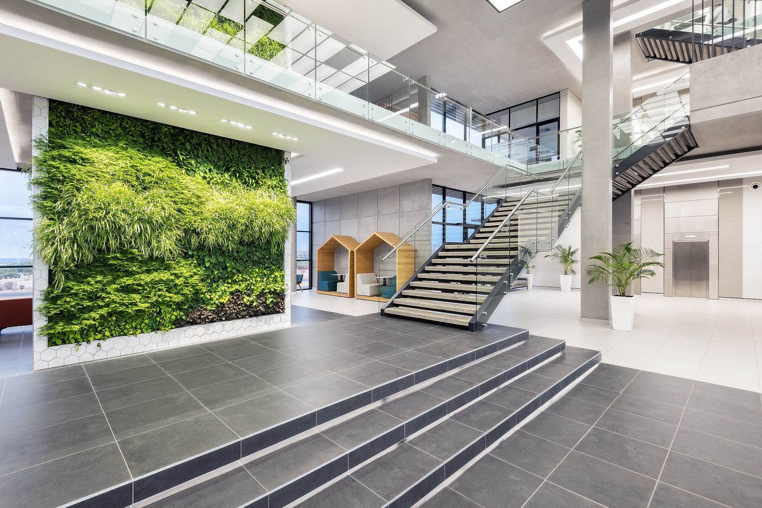 Bright modern building lobby featuring a lush vertical green wall, wide staircase, and contemporary architectural design.