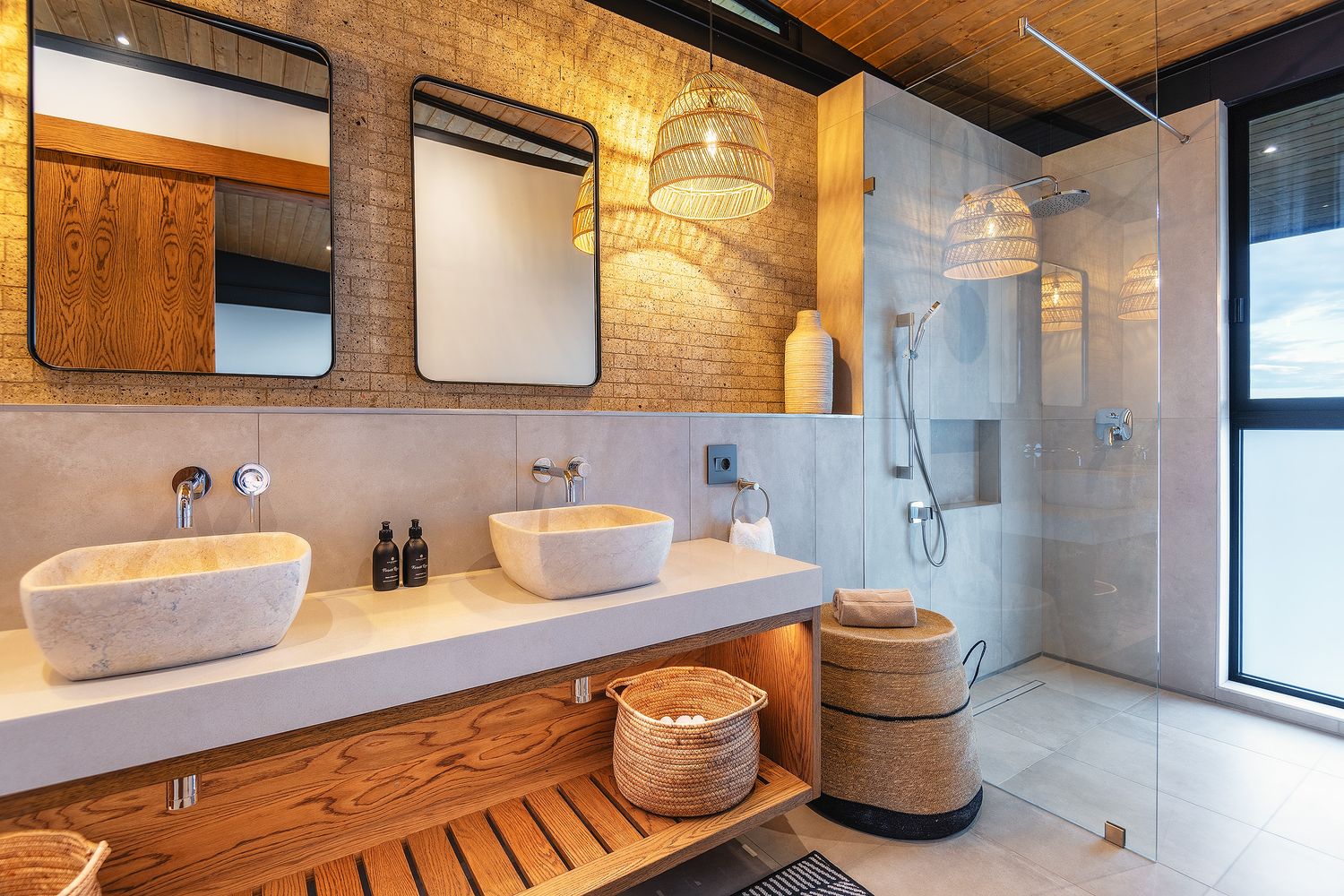 Modern double vanity bathroom with vessel sinks, woven pendant lights, brick wall, and glass shower.
