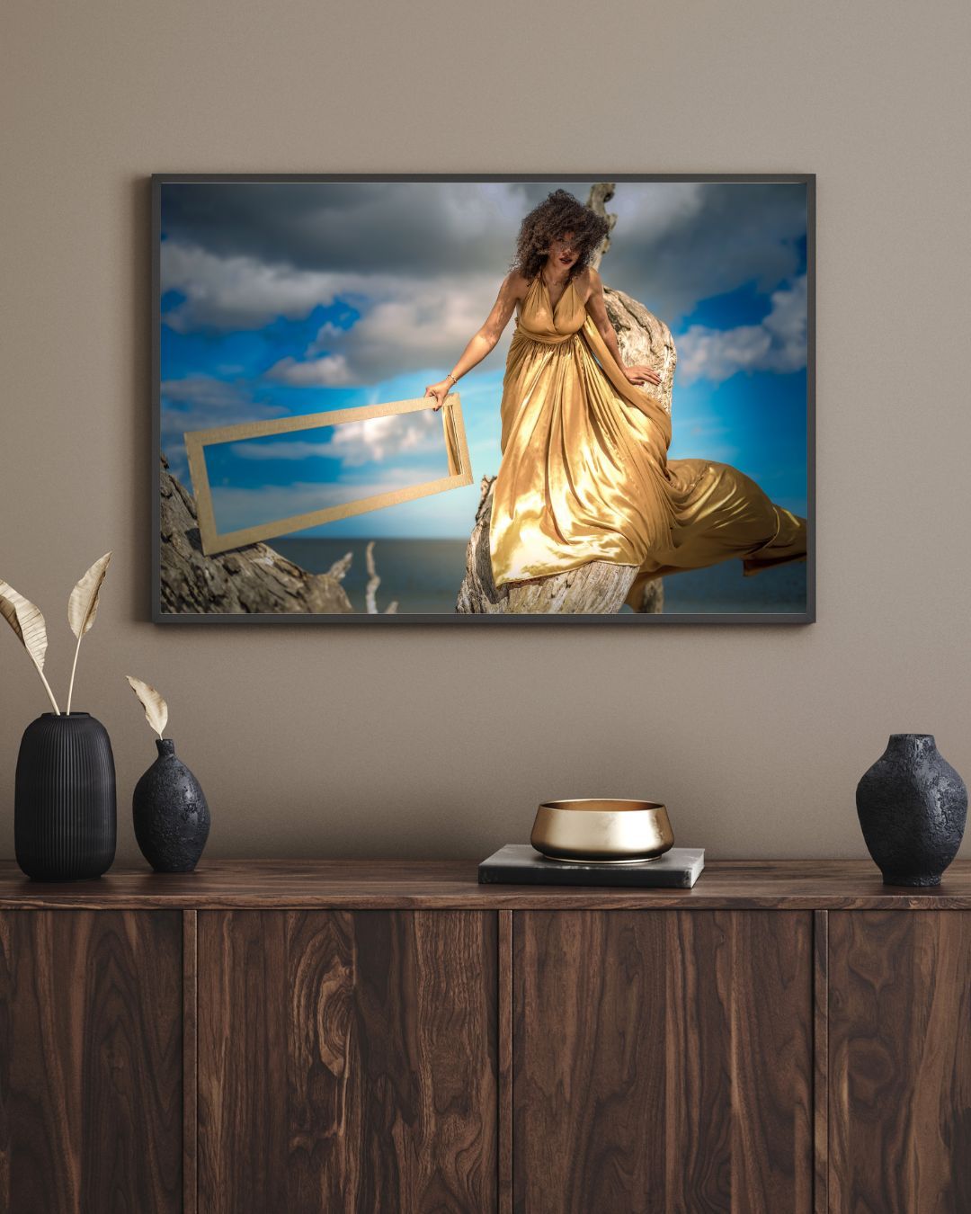 A woman in a golden gown holds a frame on rocky cliffs under dramatic blue skies in this surreal artwork.