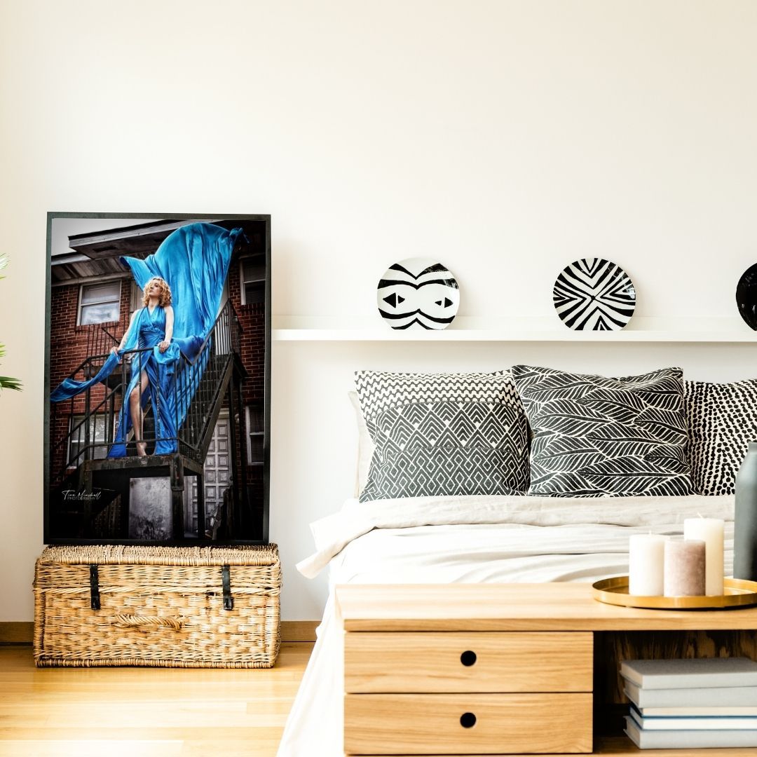 Modern bedroom with framed blue fashion flying dress art print, patterned pillows, wicker basket, and decorative wall accents.