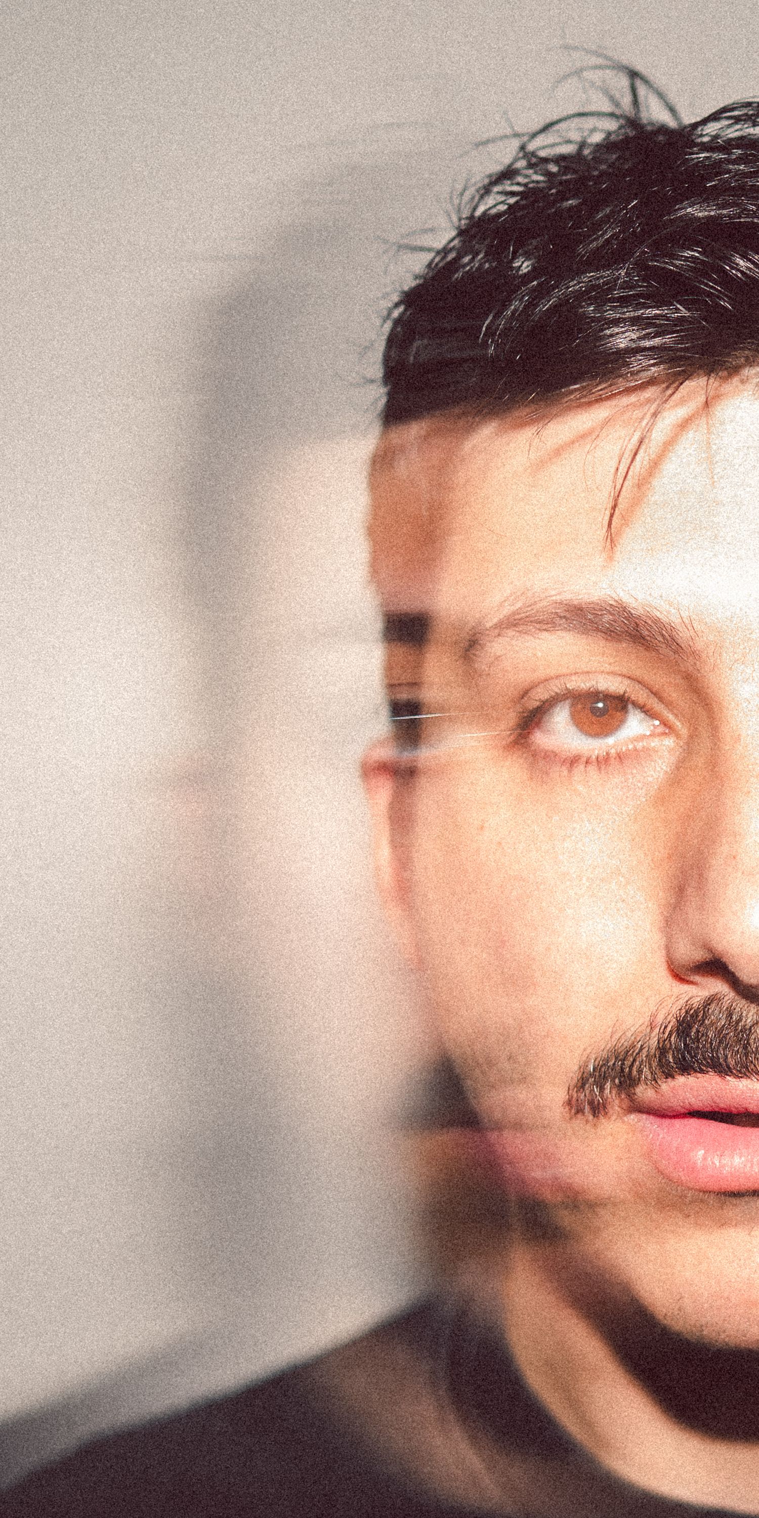Young man with mustache and dark hair in artistic double-exposure portrait photo against gray background.