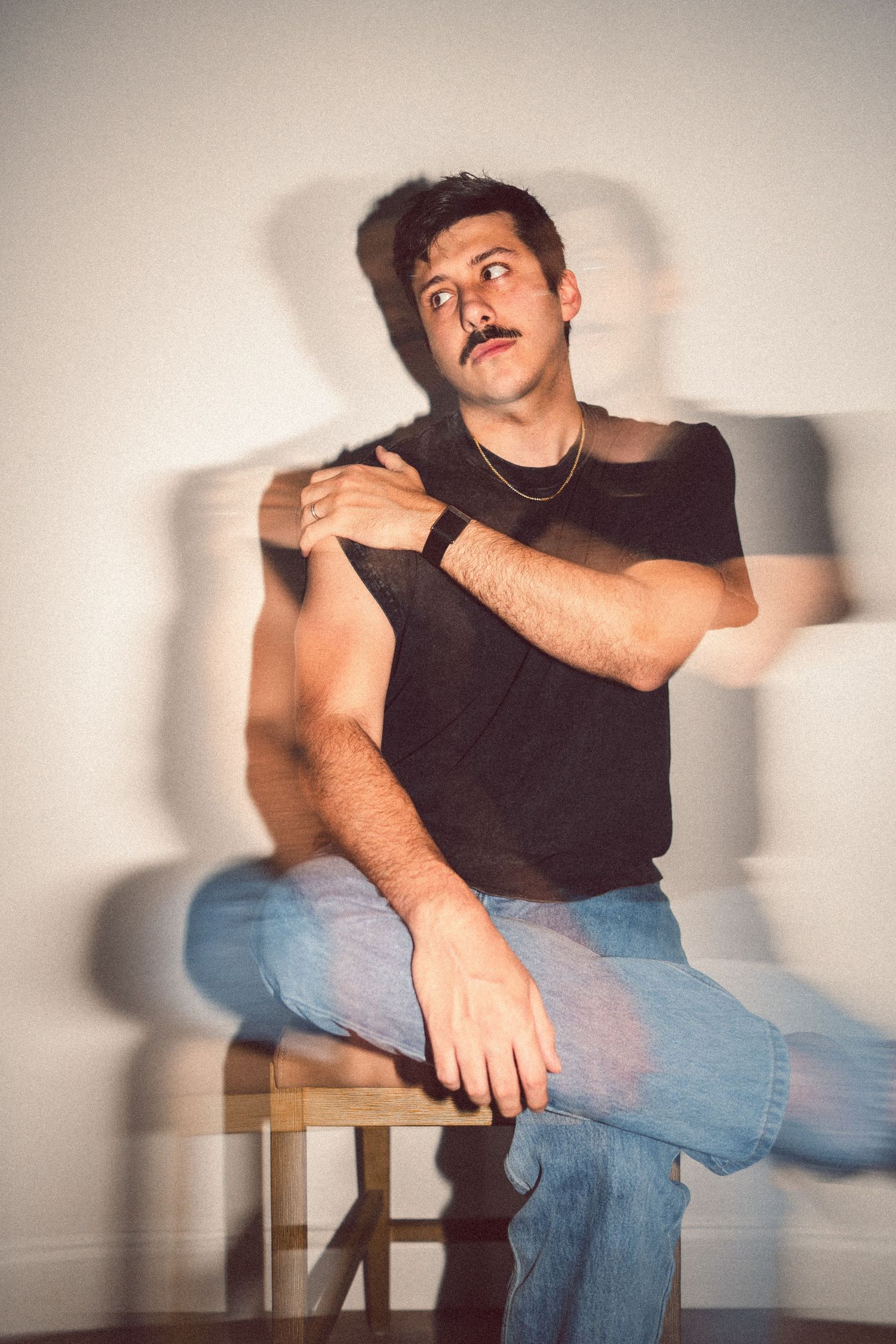 Man with mustache in black t-shirt and jeans sitting on stool with artistic motion blur double exposure effect.