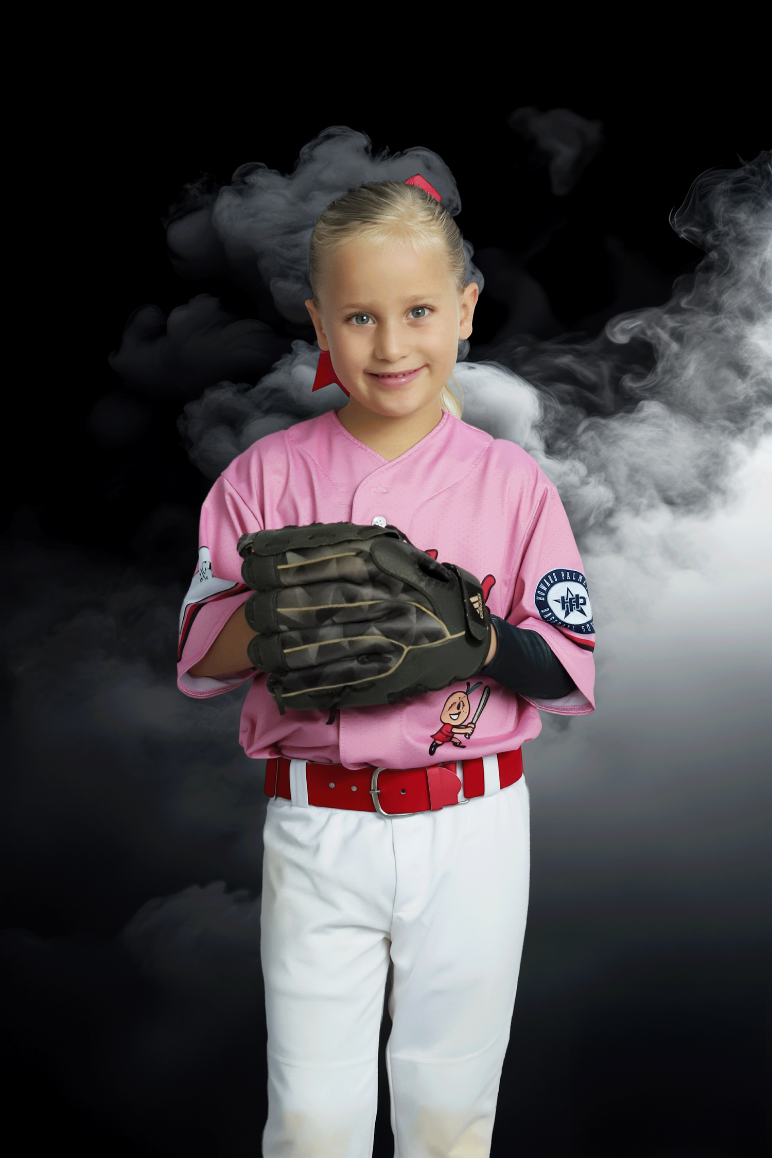 Young female baseball player in pink uniform posing with crossed arms and glove in front of white smoke background.