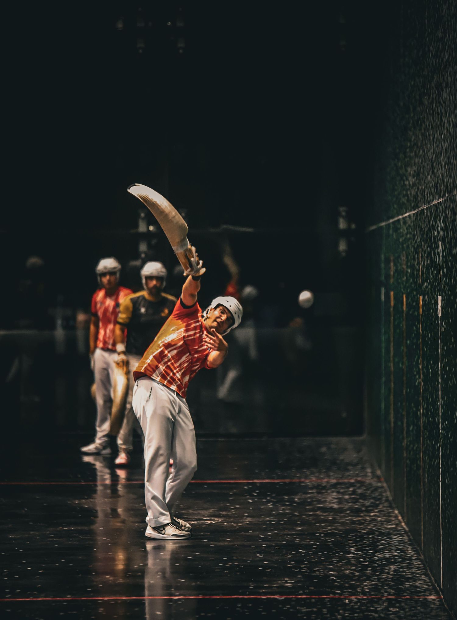Jai Alai player wearing an orange uniform throwing the ball towards the wall.