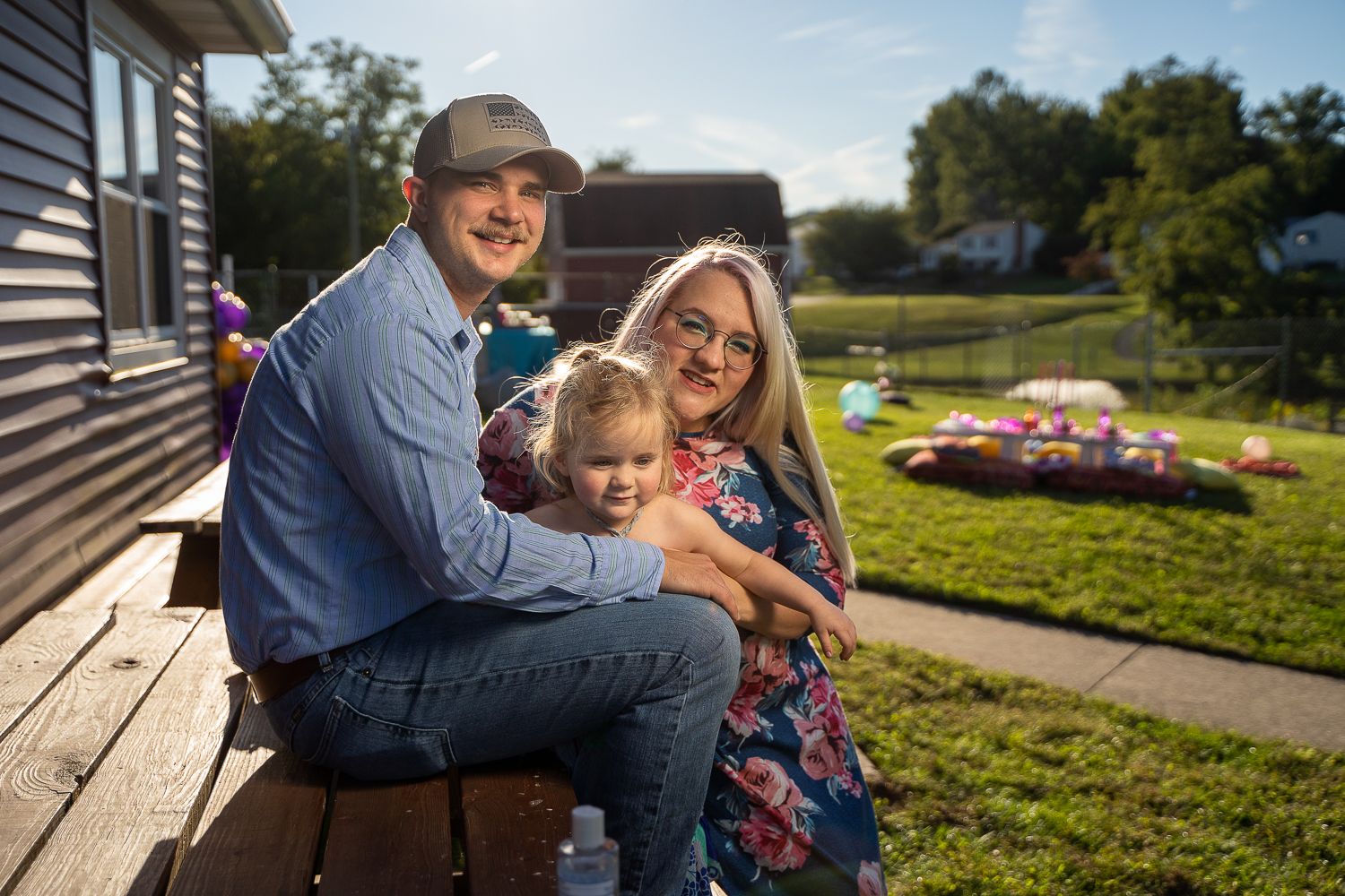 Young couple with a small child sitting on a porch in a backyard.