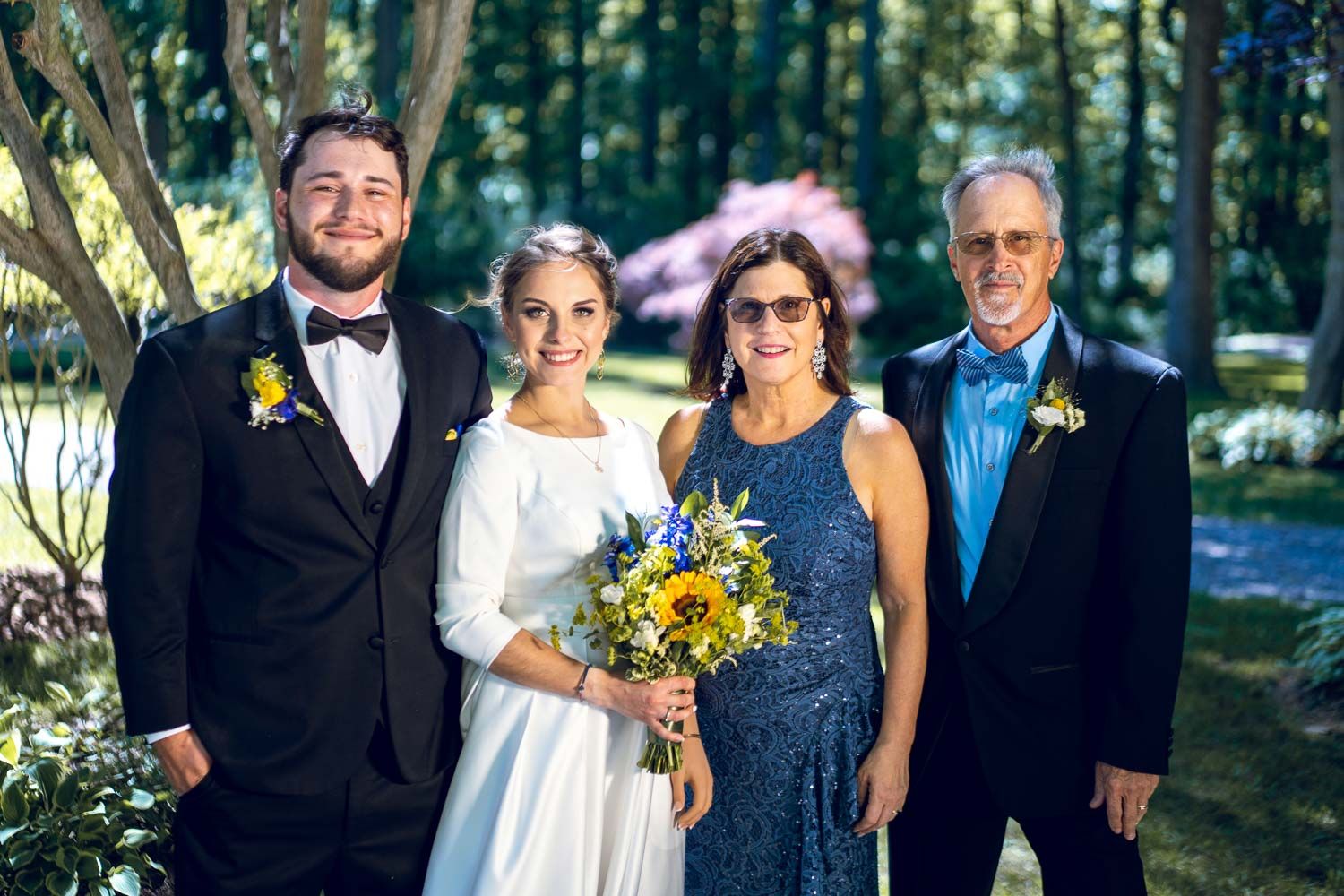Wedding party of four posing together outdoors with bride holding sunflower bouquet in garden.