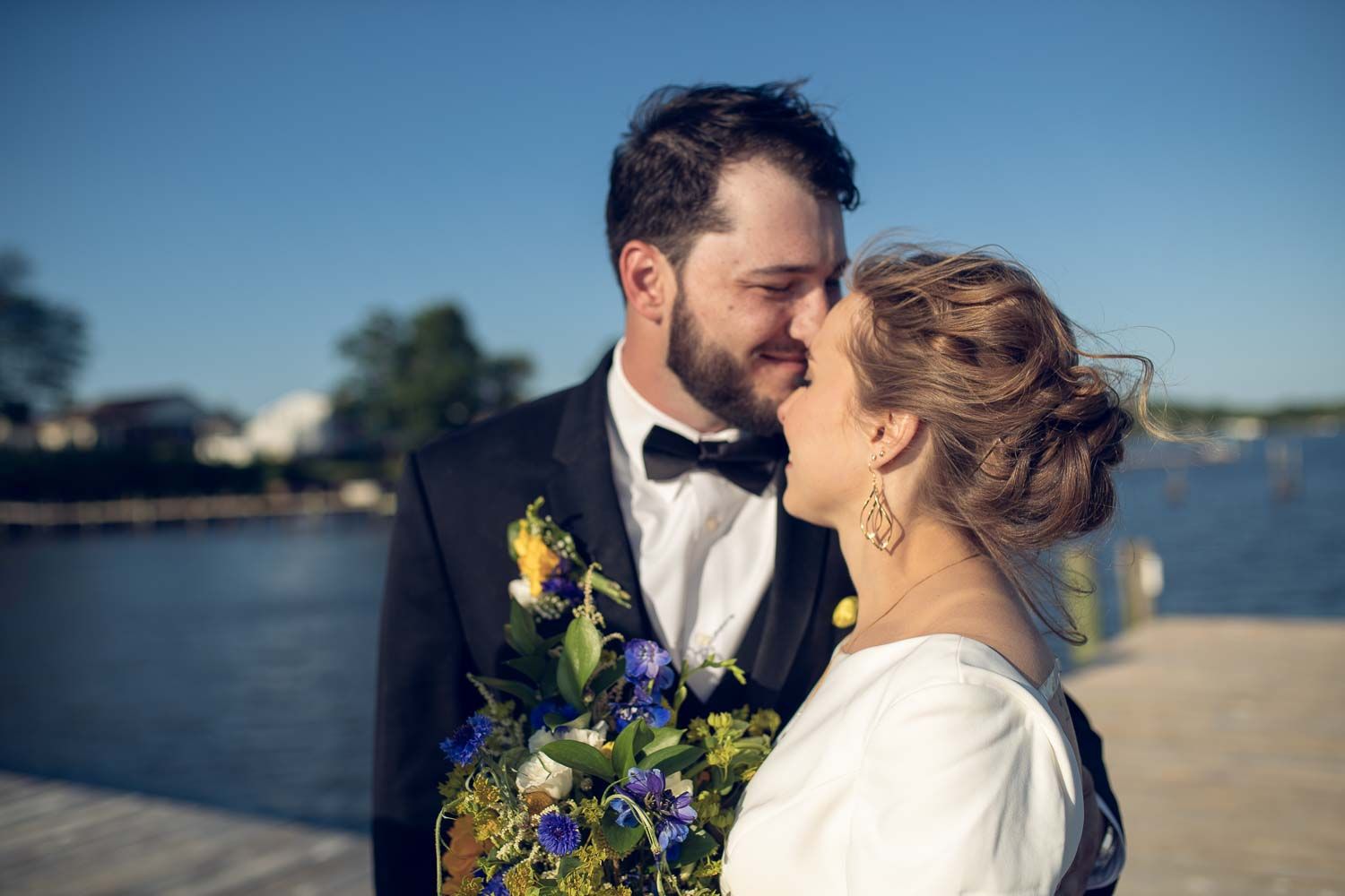 Bride and groom share a romantic almost-kiss, holding a blue and yellow wildflower wedding bouquet.