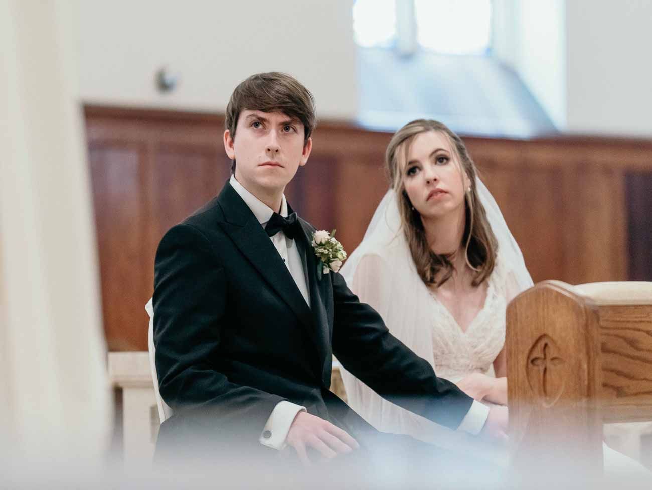Bride in white veil and groom in black tuxedo sharing an intimate moment during church ceremony.