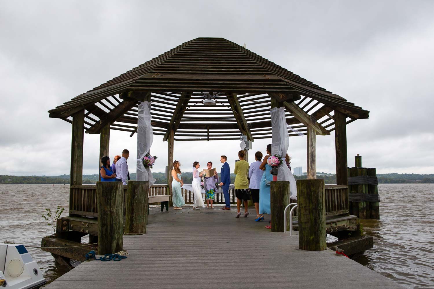 Small intimate wedding ceremony under a wooden gazebo on a pier overlooking calm water.