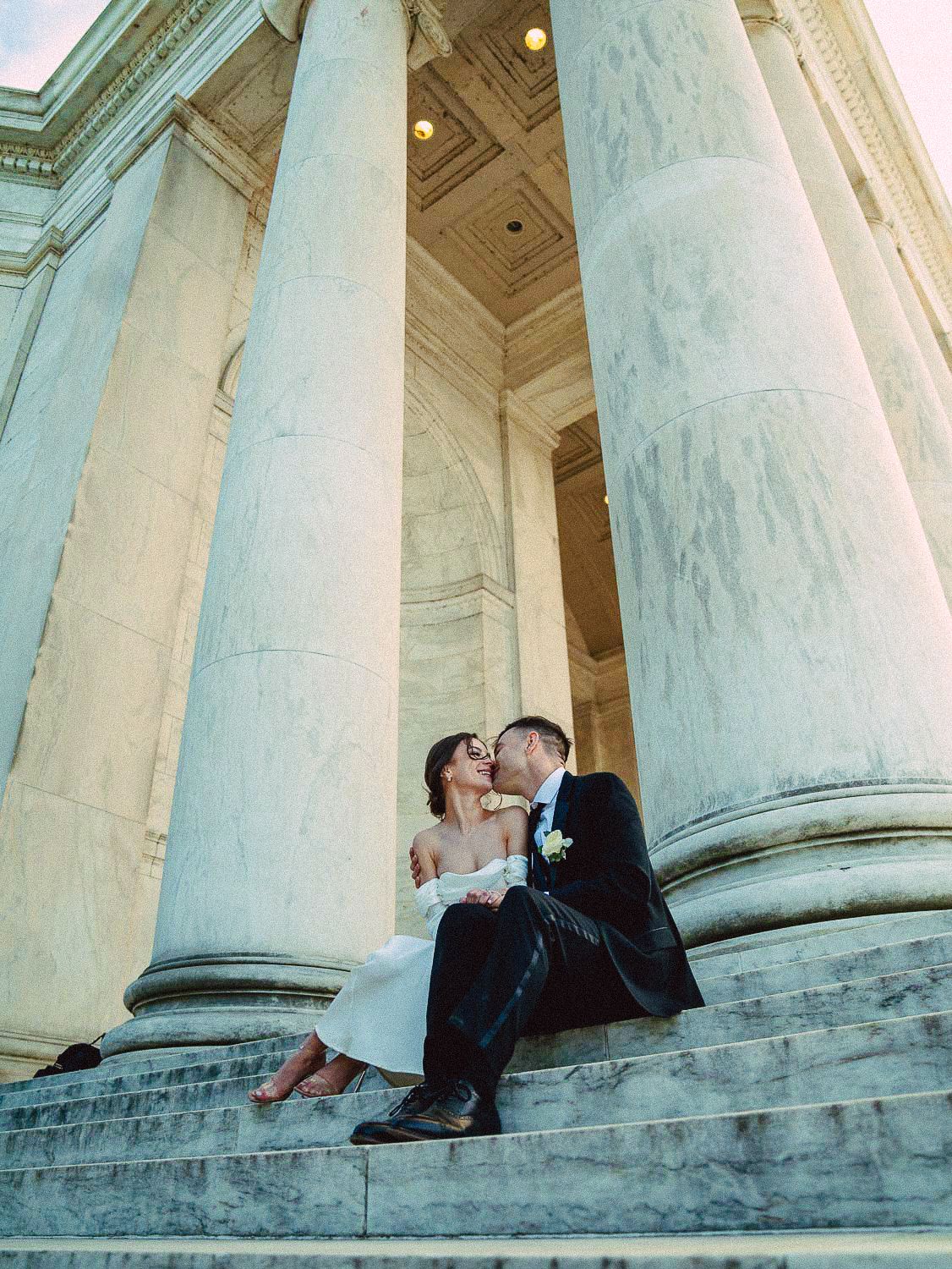 Bride and groom share a kiss on the steps of the Jefferson Memorial, surrounded by grand marble columns.