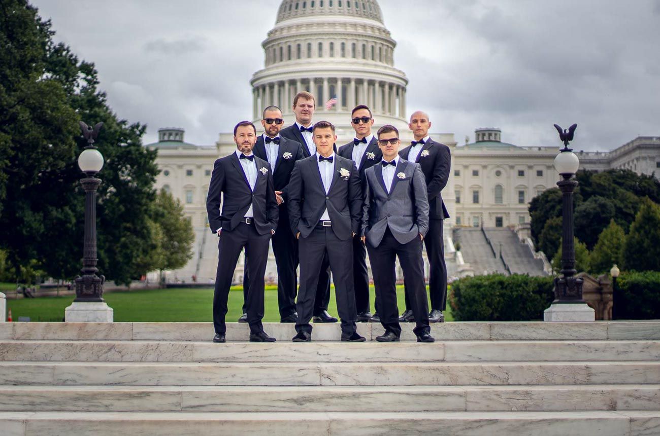Group of groomsmen in dark suits pose on steps of US Capitol Building.
