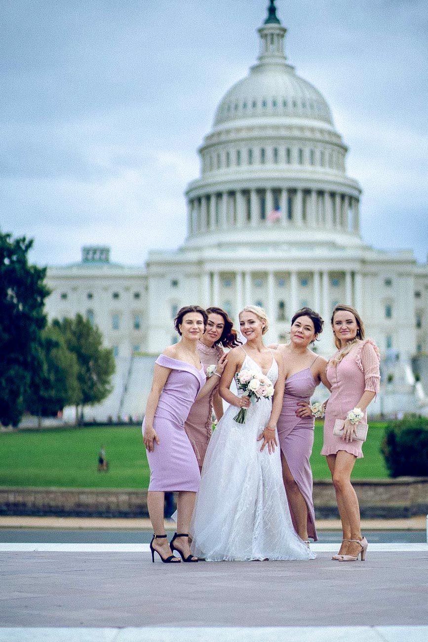 Bride holding white bouquet standing with four bridesmaids in pink dresses before the US Capitol.