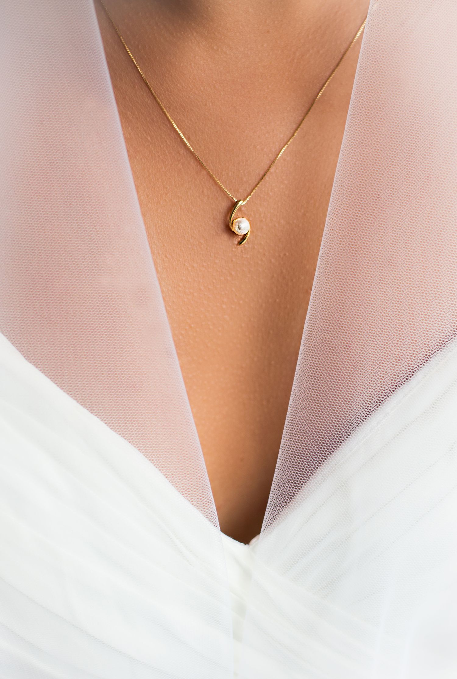 A close-up of a gold pearl pendant necklace worn by a bride in a white wedding dress.