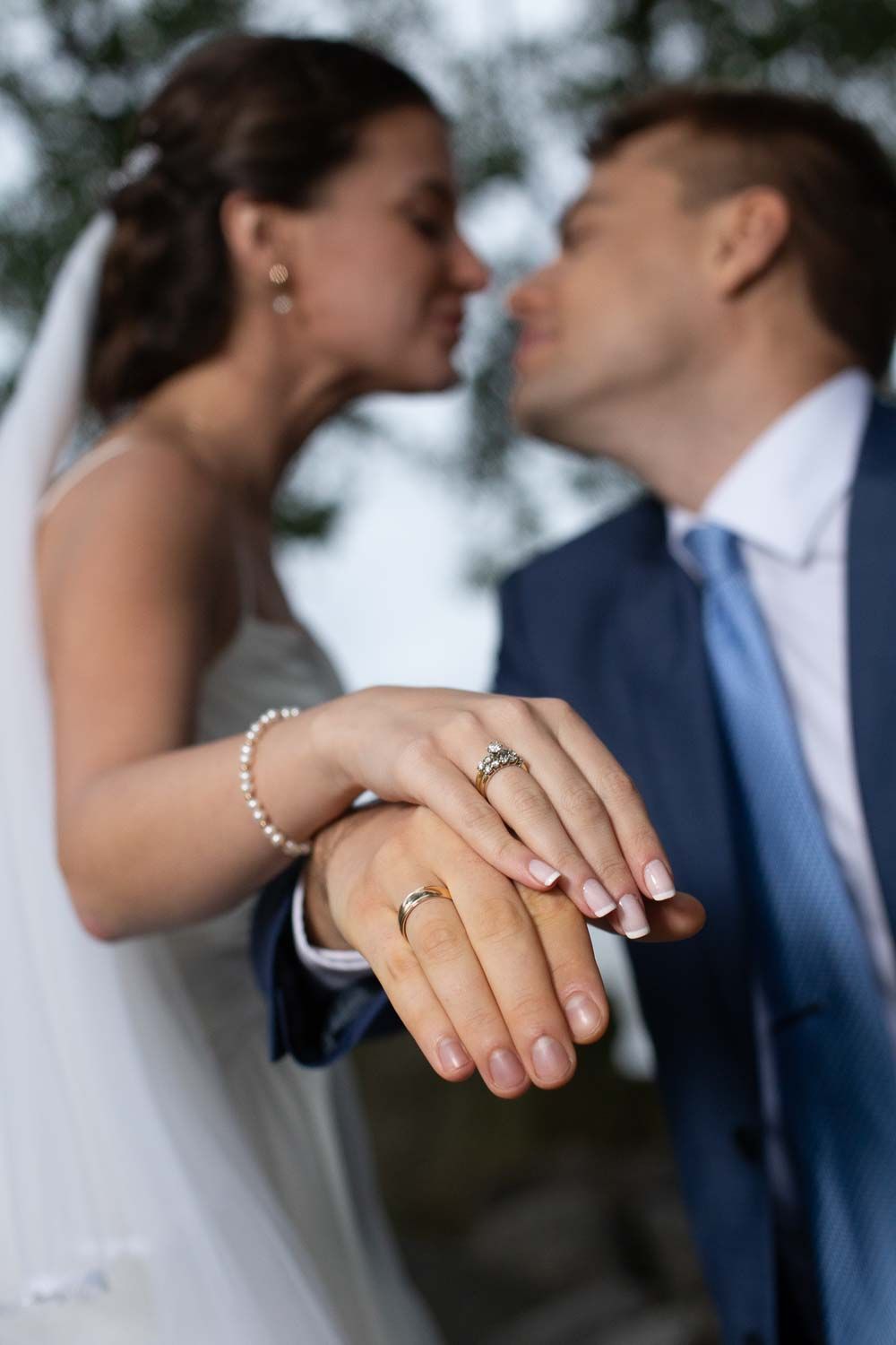 Newlyweds kissing while displaying their wedding rings with focus on the rings in the foreground.