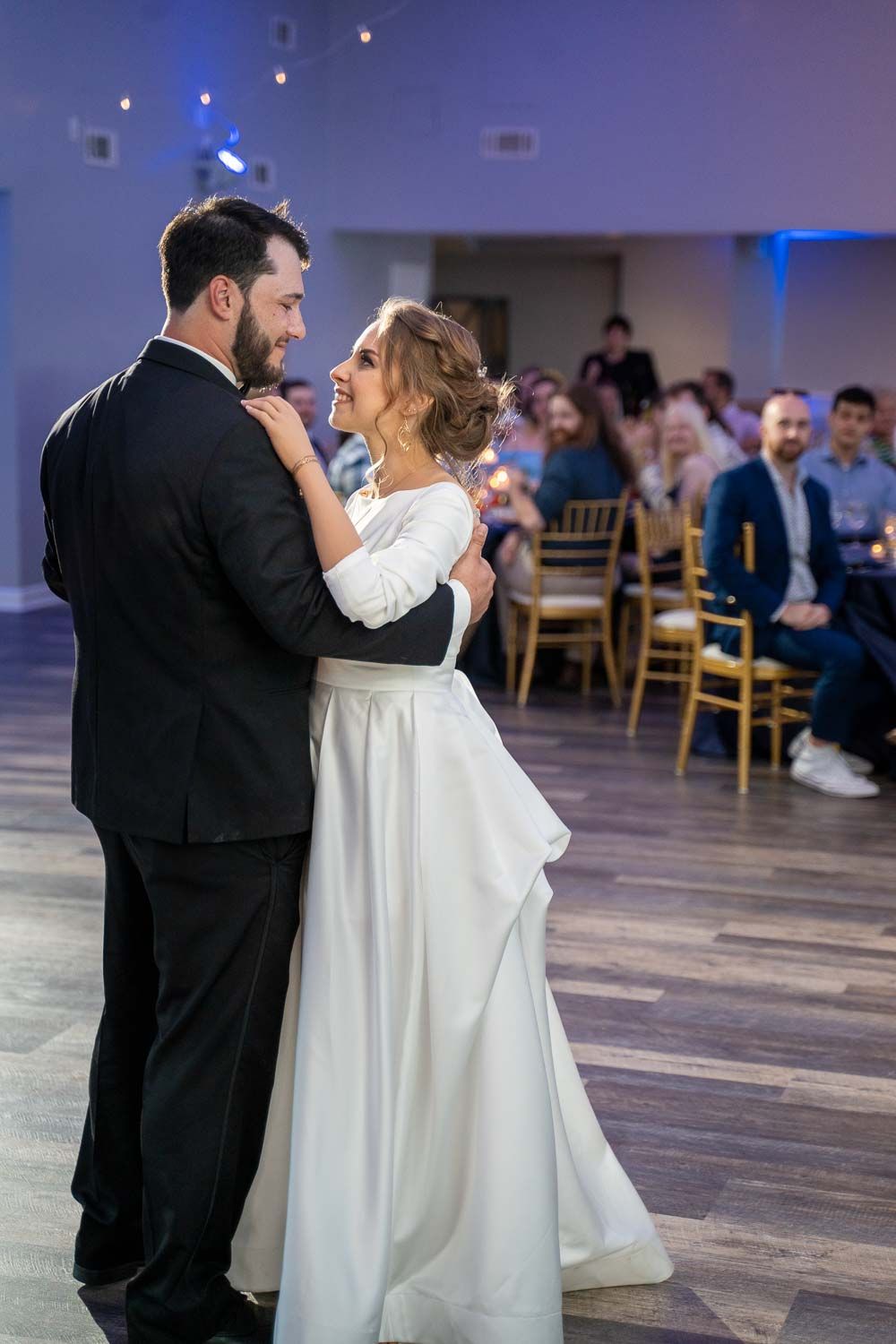 Bride and groom sharing first dance while wedding guests watch in elegant reception venue.