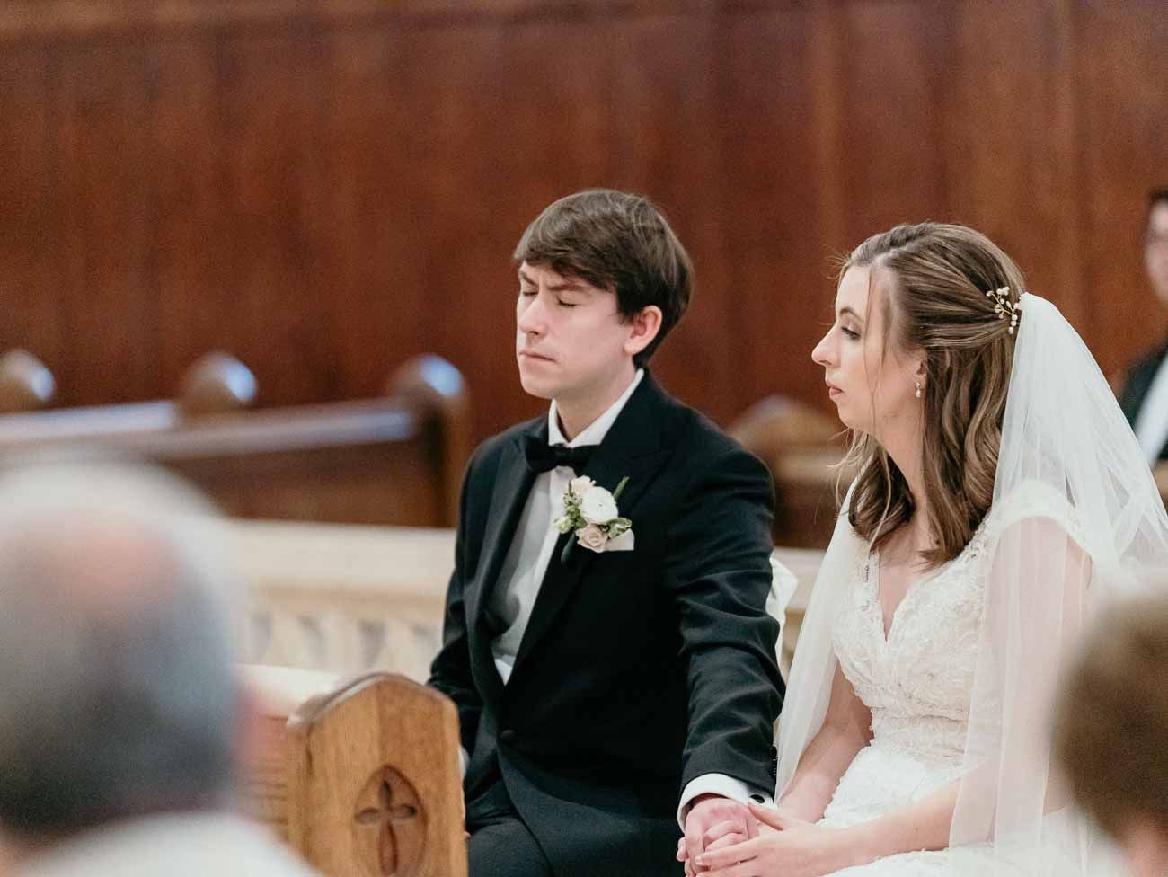Bride and groom hold hands while seated at the altar during their Catholic church wedding ceremony.