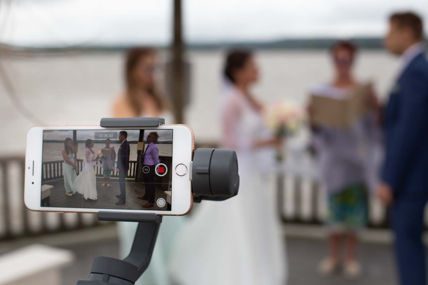 Wedding ceremony being recorded on a smartphone with gimbal stabilizer on a waterfront deck.