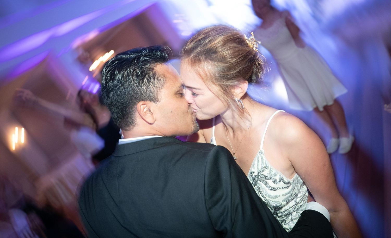 Couple shares a romantic kiss on the dance floor during their wedding reception with purple lighting.