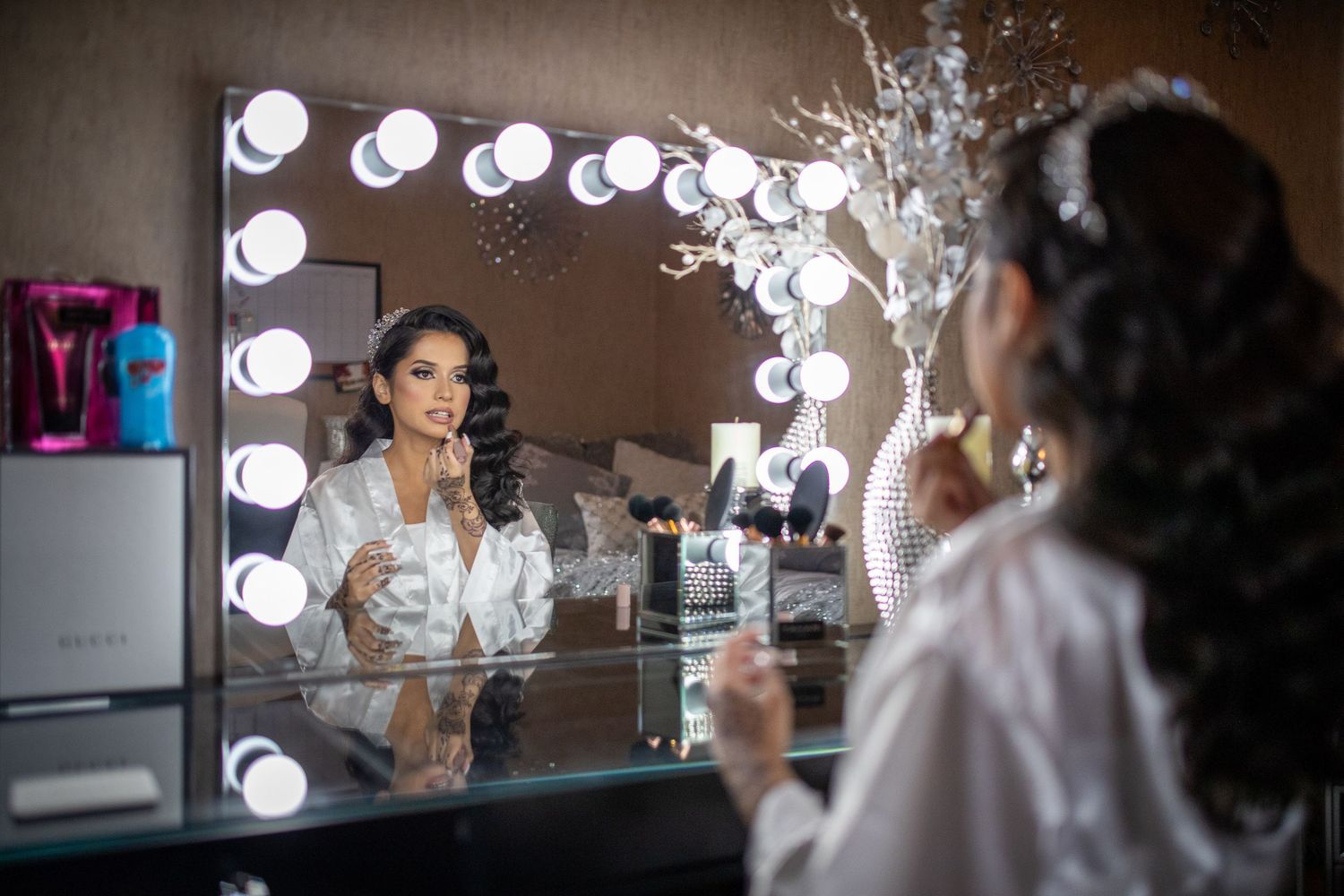 Beautiful bride applies makeup while seated at a lighted vanity mirror before her wedding.