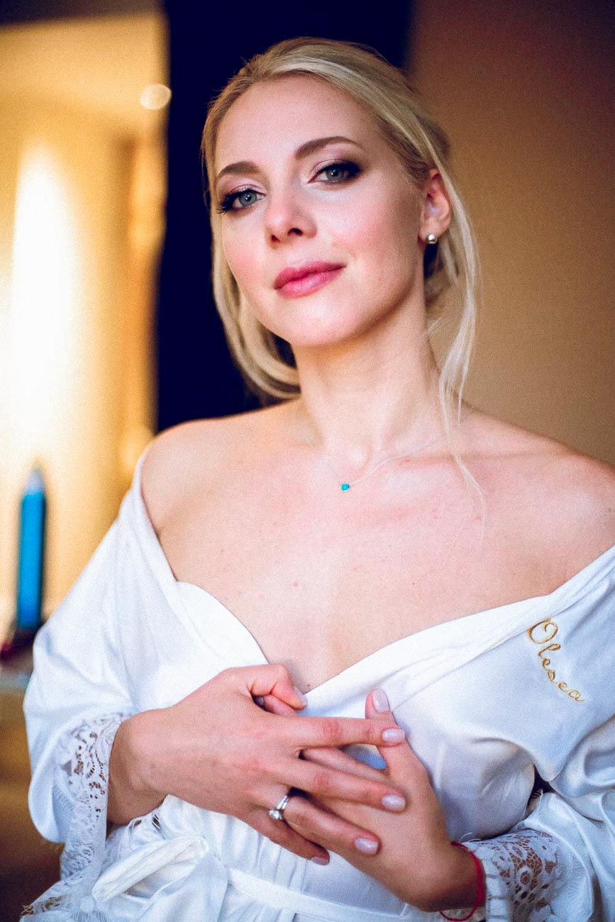 Beautiful blonde bride in white robe with turquoise necklace and engagement ring.