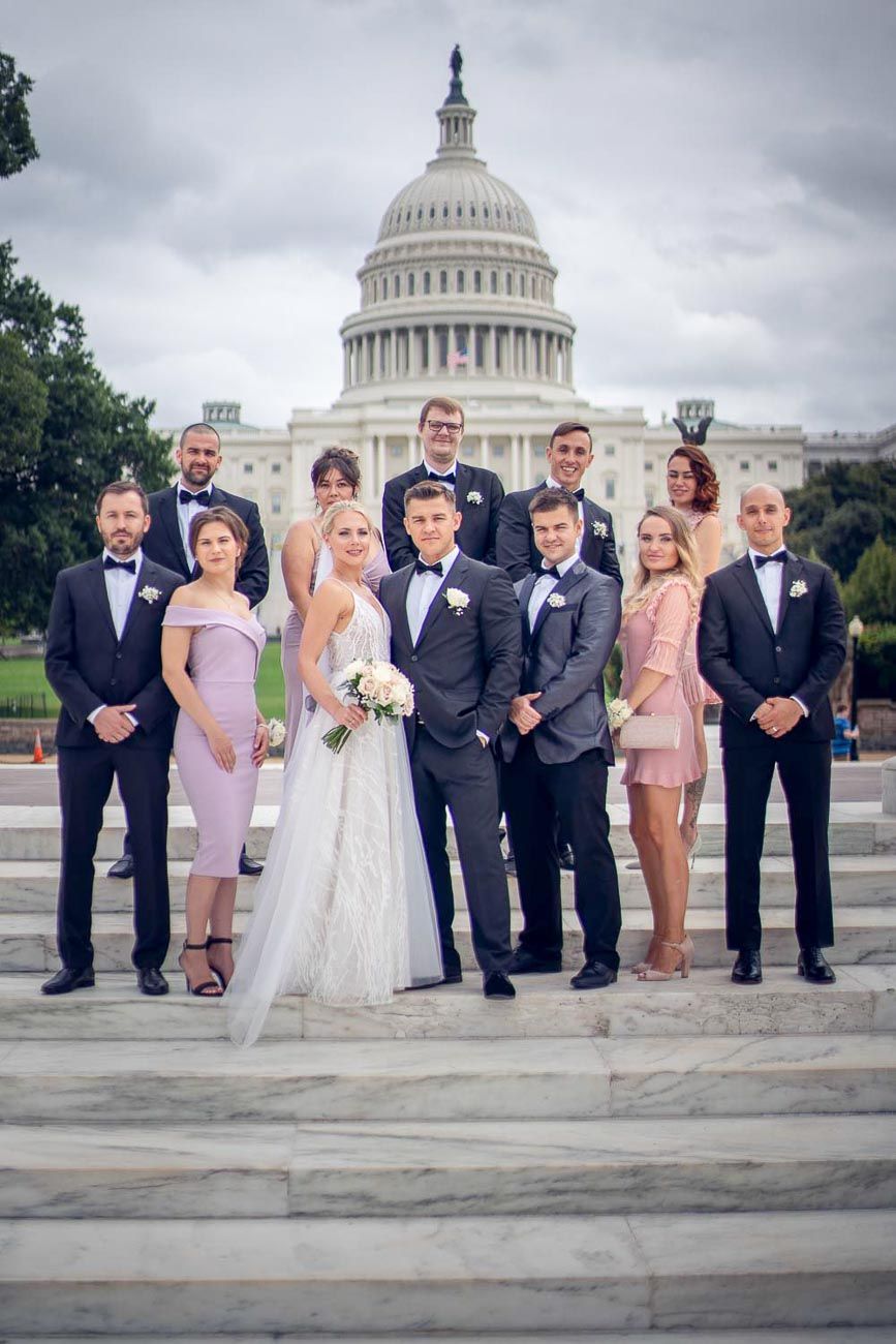 Wedding party with bride, groom, groomsmen in tuxedos and bridesmaids posing on US Capitol steps.