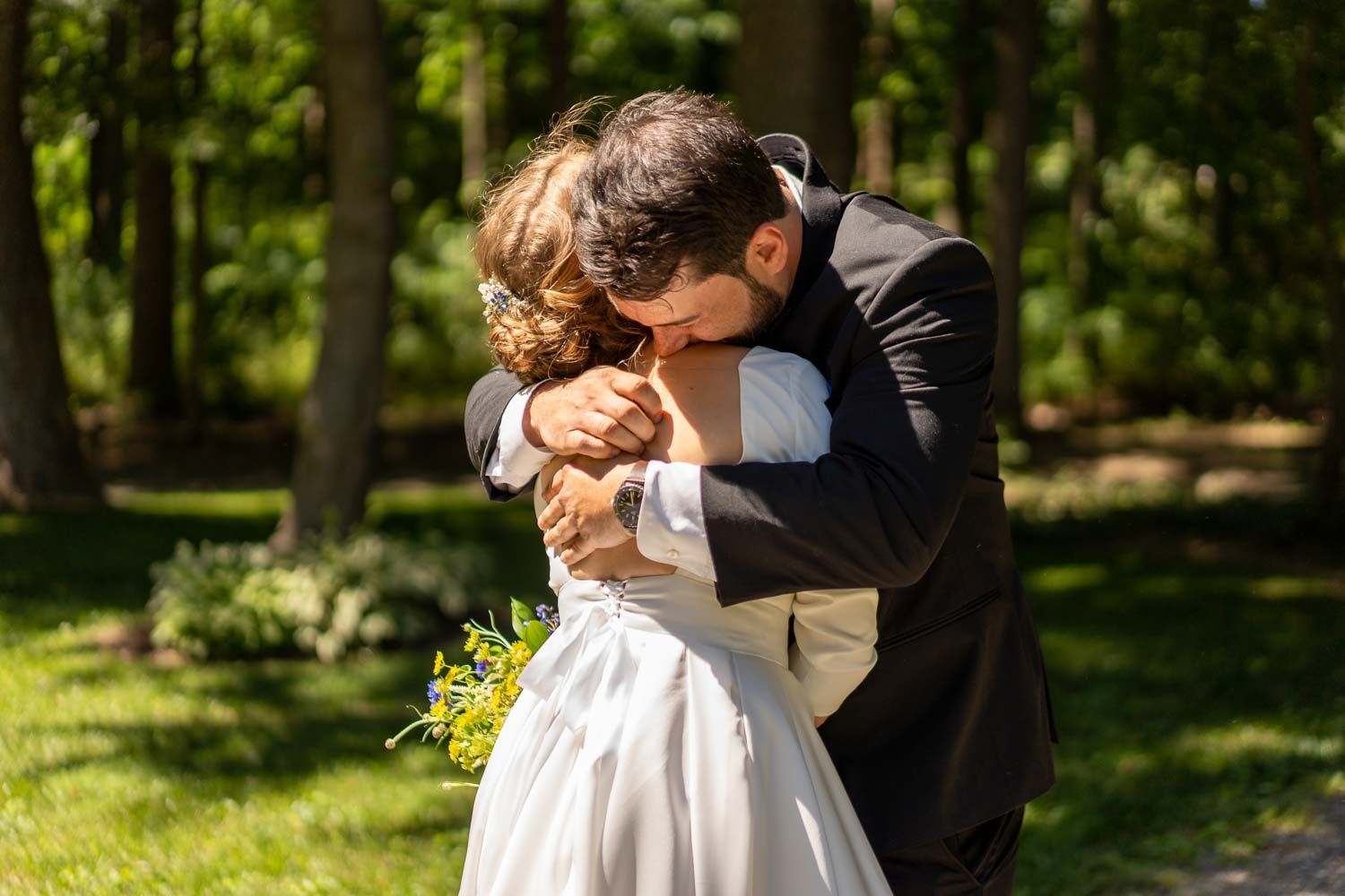 Bride and groom share a tender embrace in a lush green outdoor wedding setting.