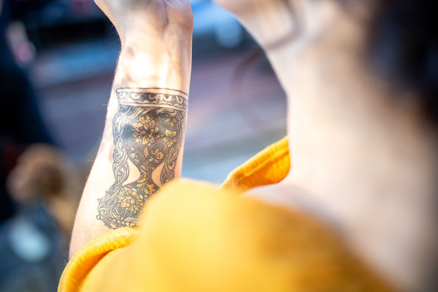 Close-up of decorative black henna-style tattoo on woman's forearm in yellow dress.