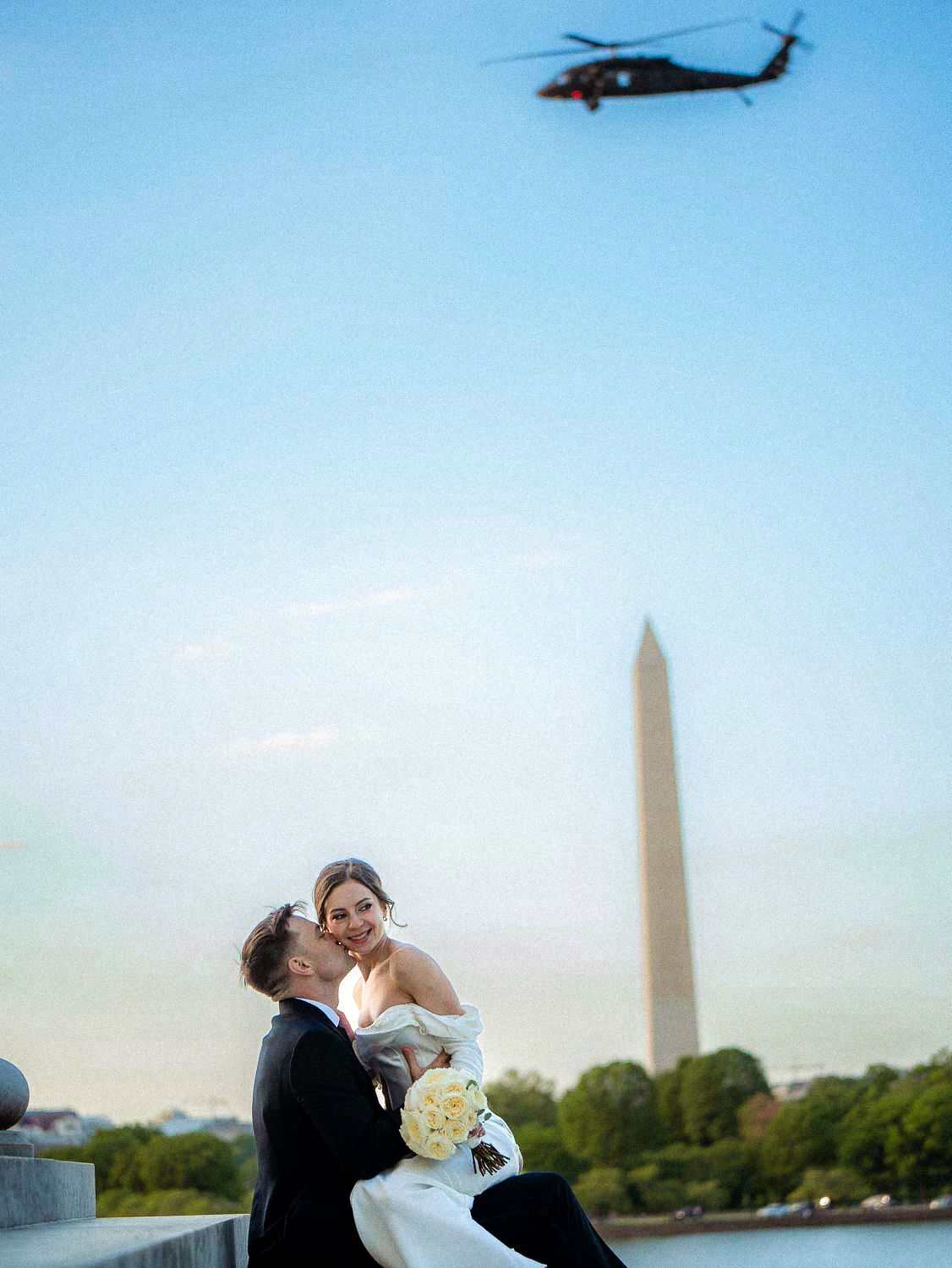 Wedding couple share a romantic moment on steps with Washington Monument and helicopter in background.