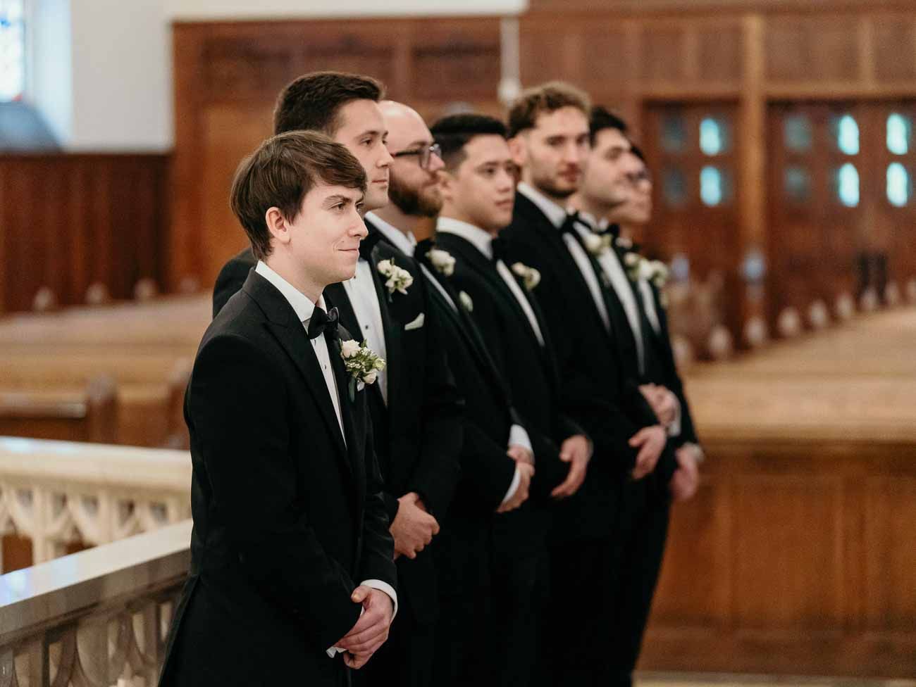 Groomsmen in black tuxedos standing at altar during wedding.