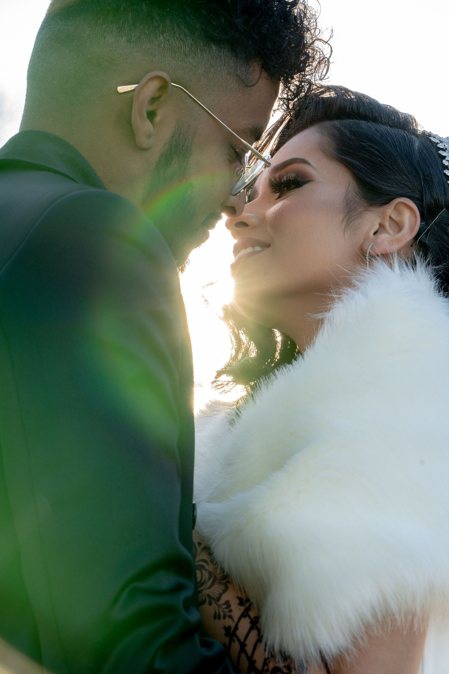 A couple in wedding attire share an intimate moment with sunlight glowing behind them.