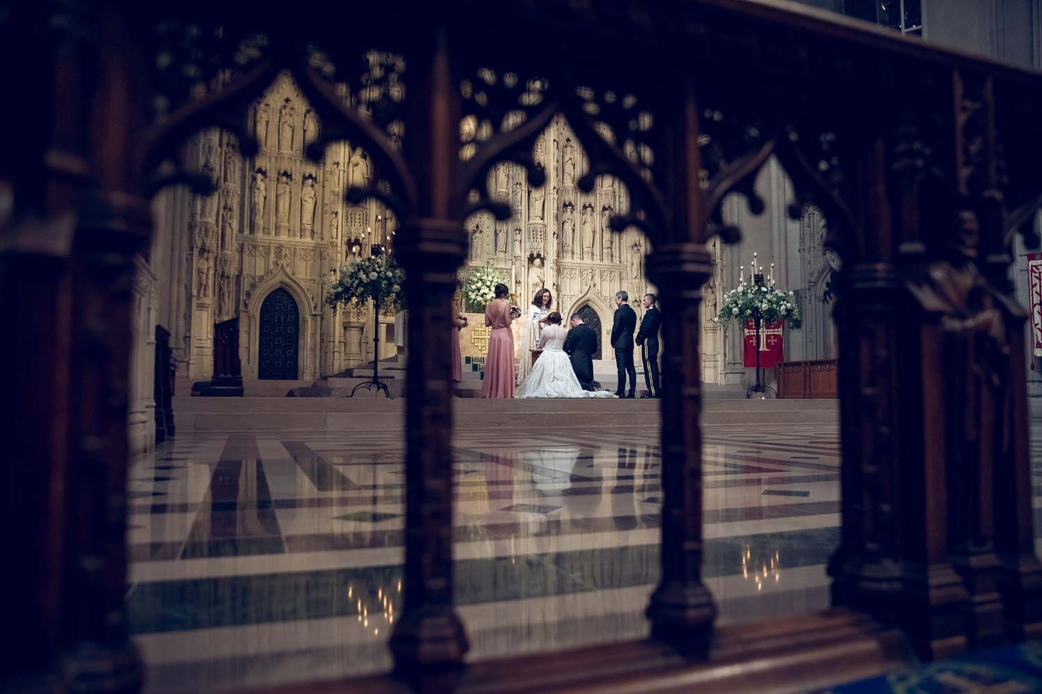Wedding ceremony captured through ornate Gothic cathedral woodwork with dramatic architectural framing.