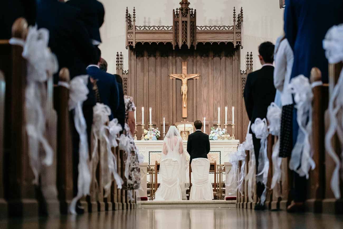 Bride and groom kneel at the altar during a traditional Catholic wedding ceremony with crucifix.